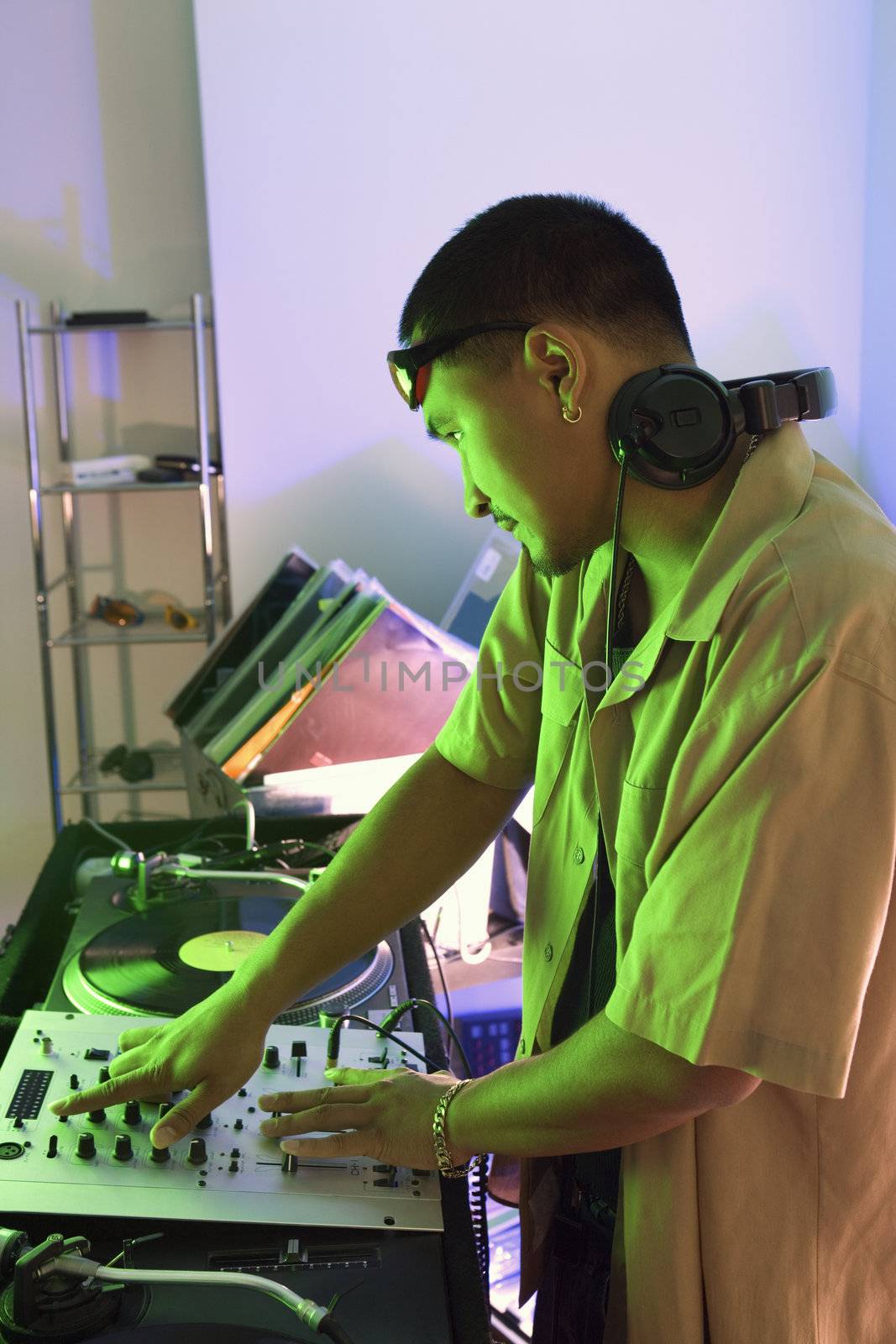 Profile of Asian young adult male DJ with mixing equipment, turntables and headphones.