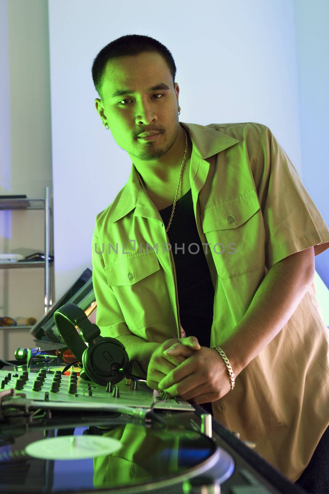 Asian young adult male DJ leaning on turntable looking at viewer.