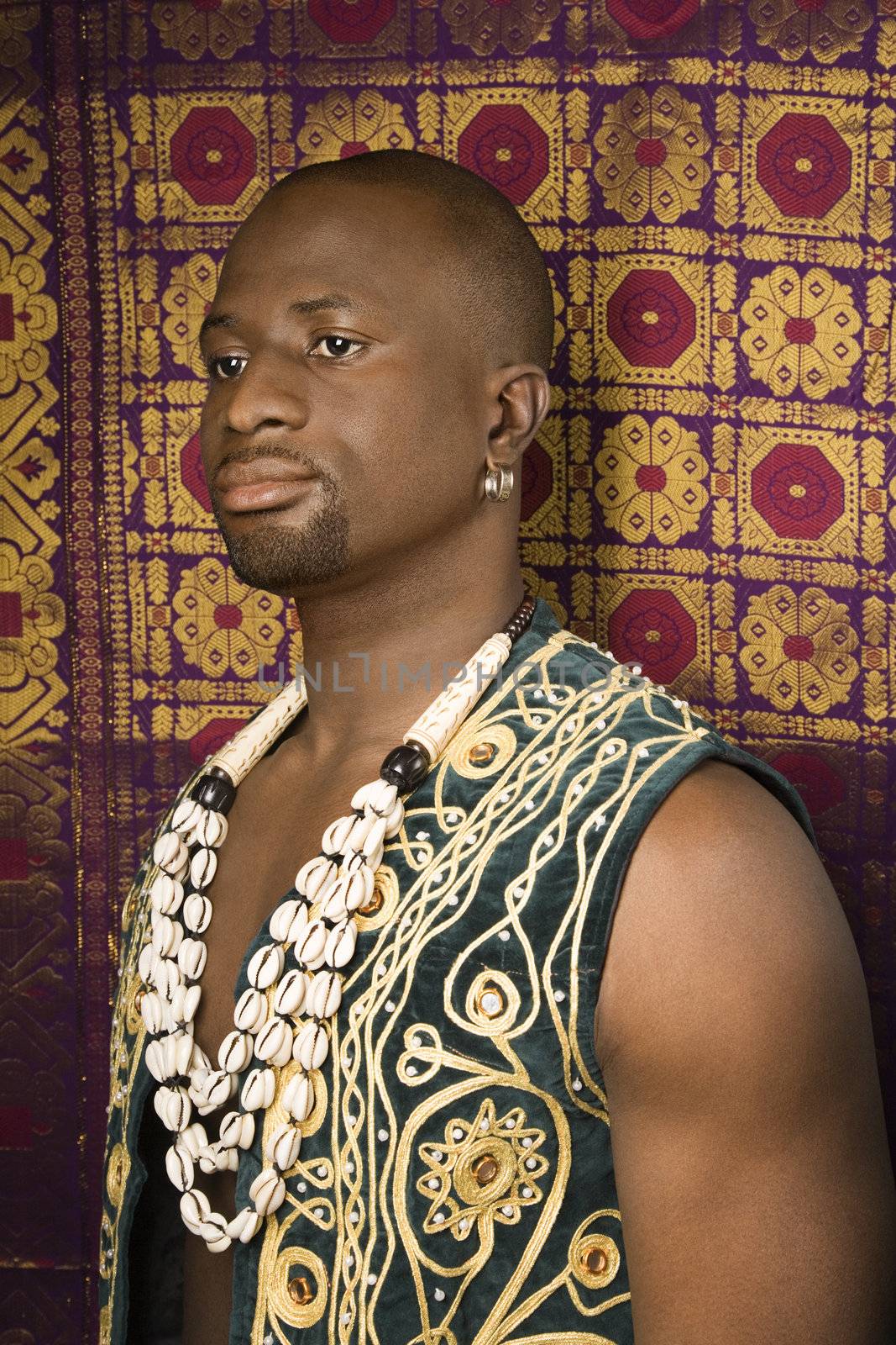 Side view portrait of African-American mid-adult man wearing embroidered African vest and beads.