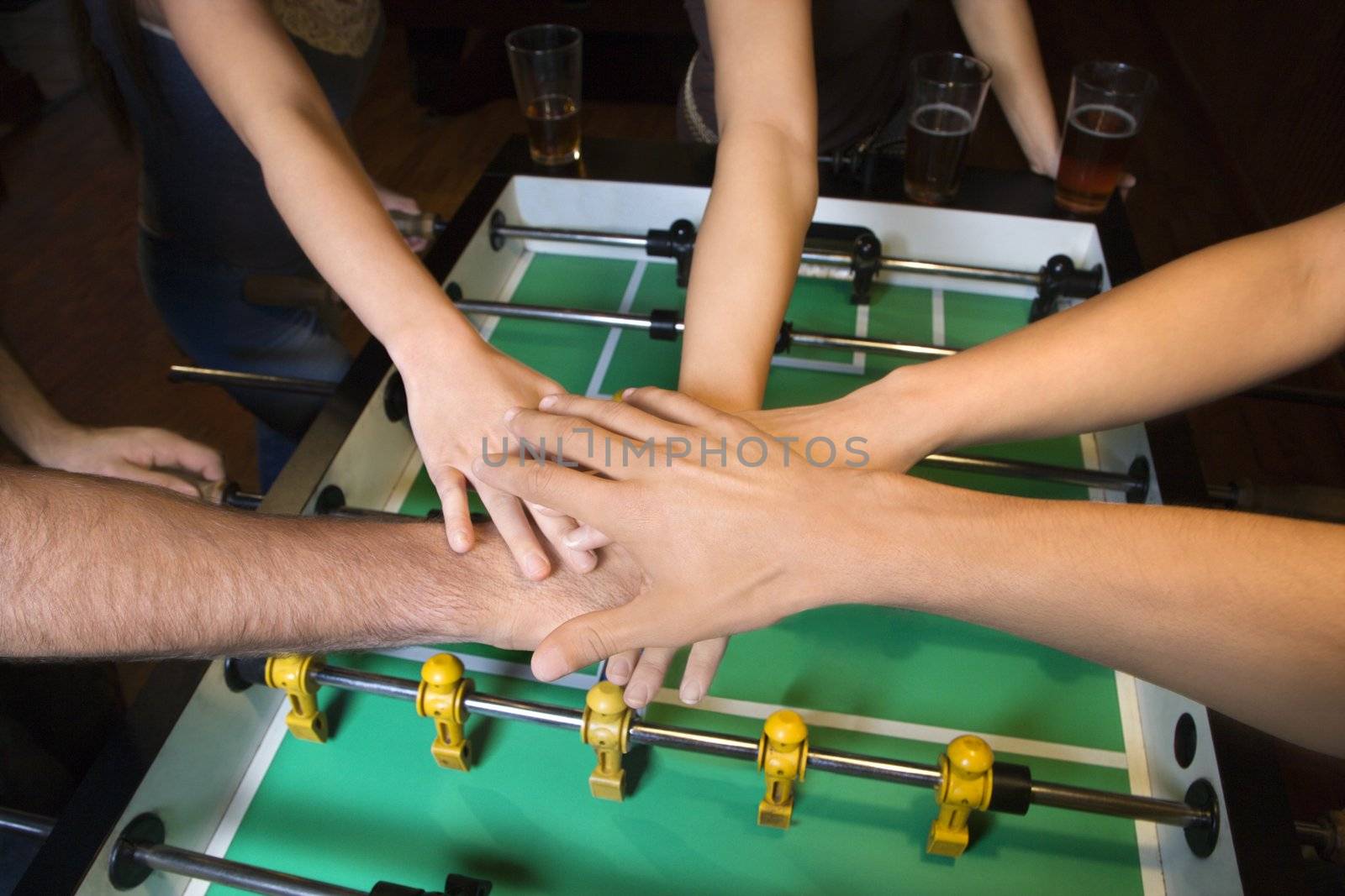 Group of young friends clasping hands in solidarity over foosball table.