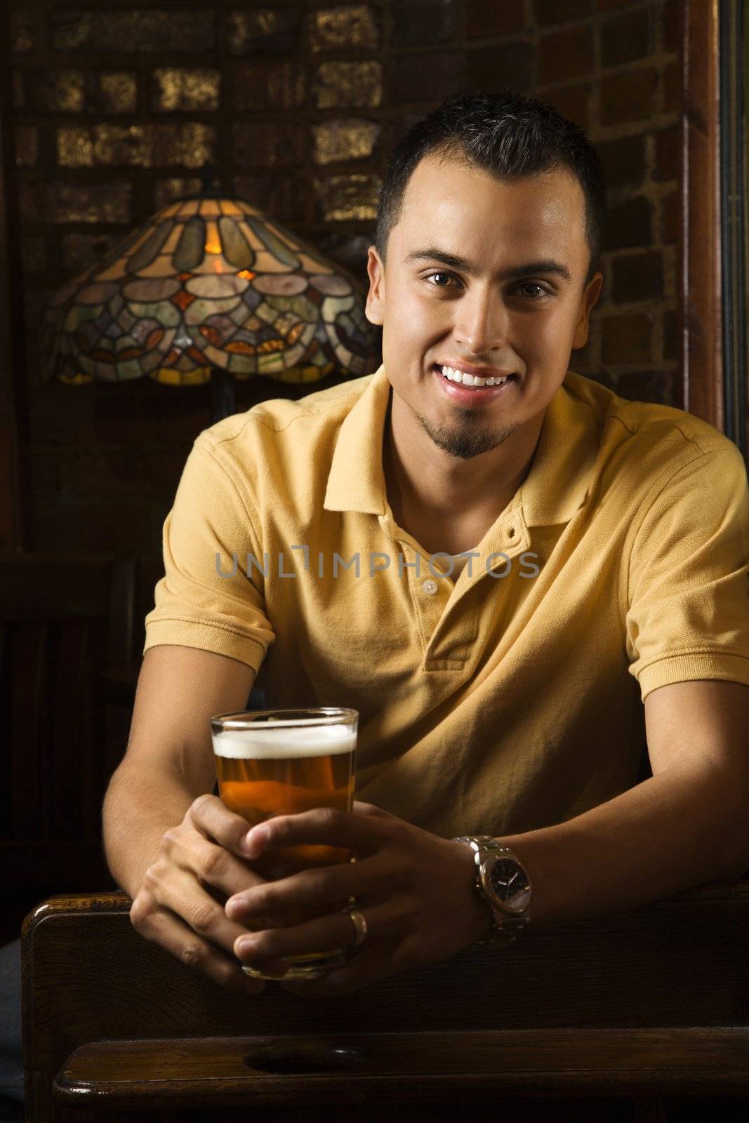 Portrait of smiling young Hispanic man holding beer in pub.
