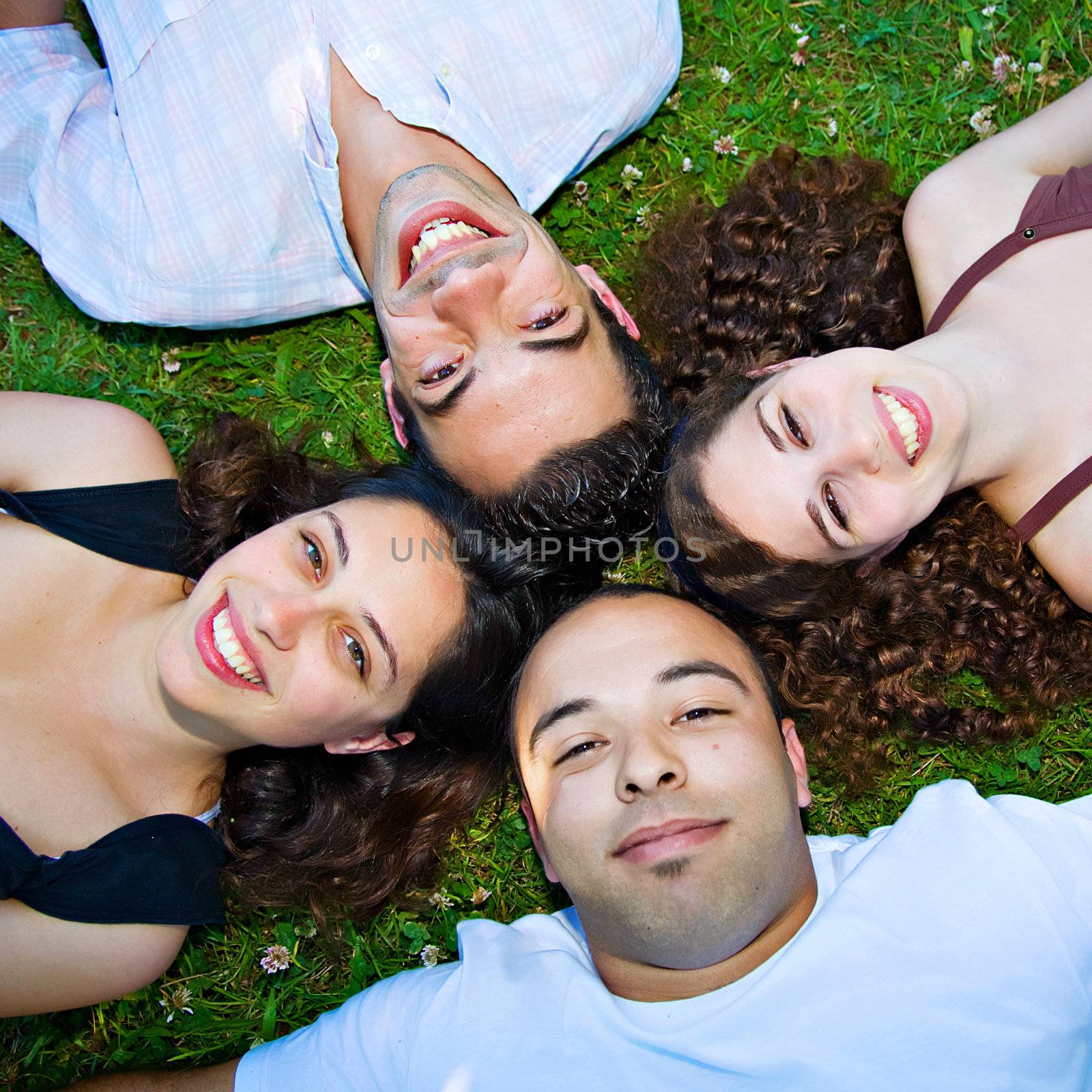 Four young people laying down in the grass, smiling.