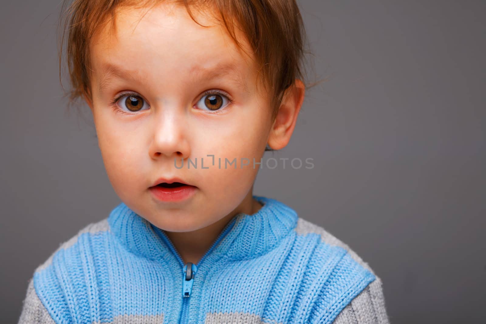 Closeup portrait of a little surprised boy in a blue sweater, open attentive look