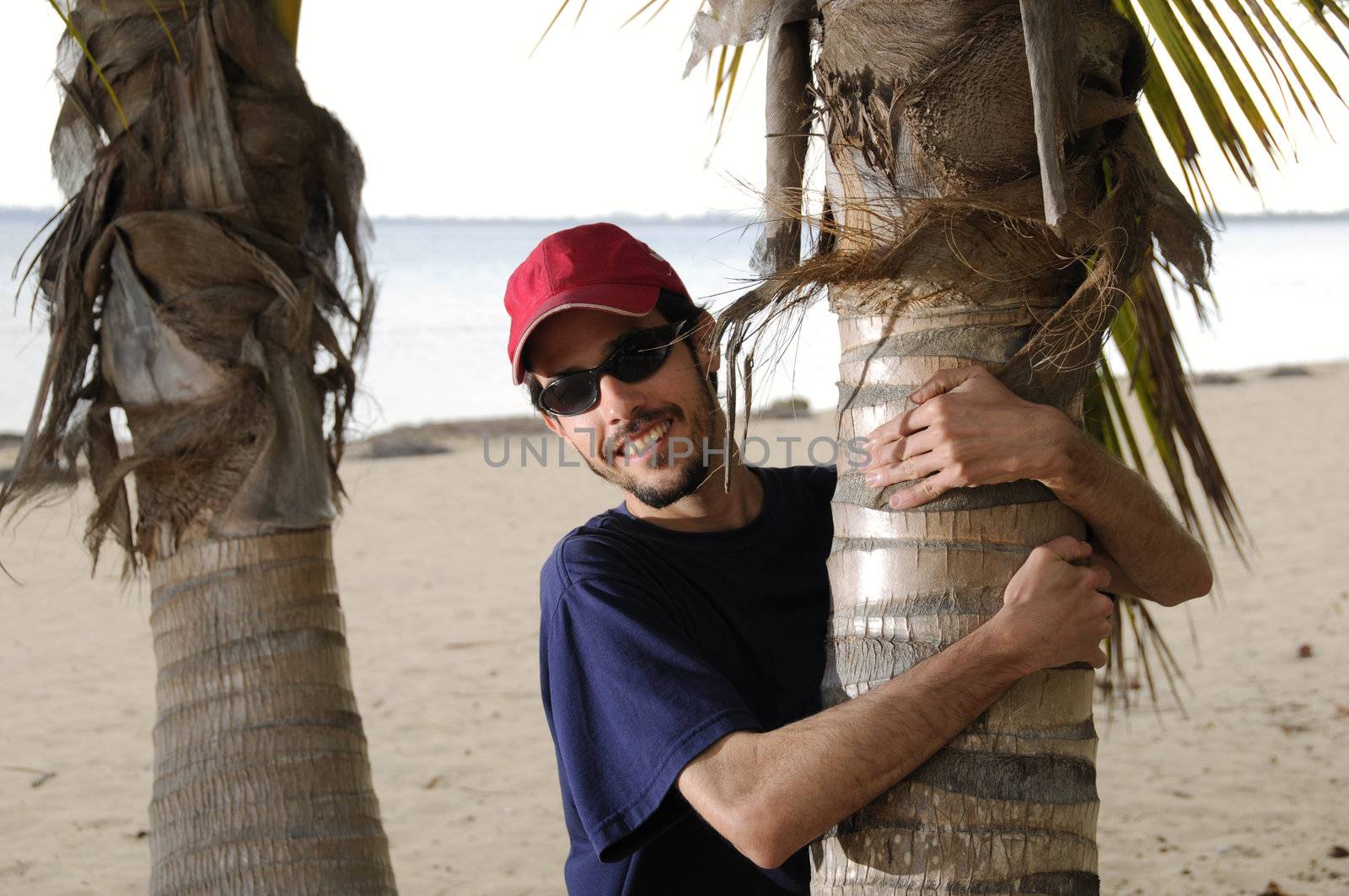 Man embracing coconut palm tree trunk on a beach