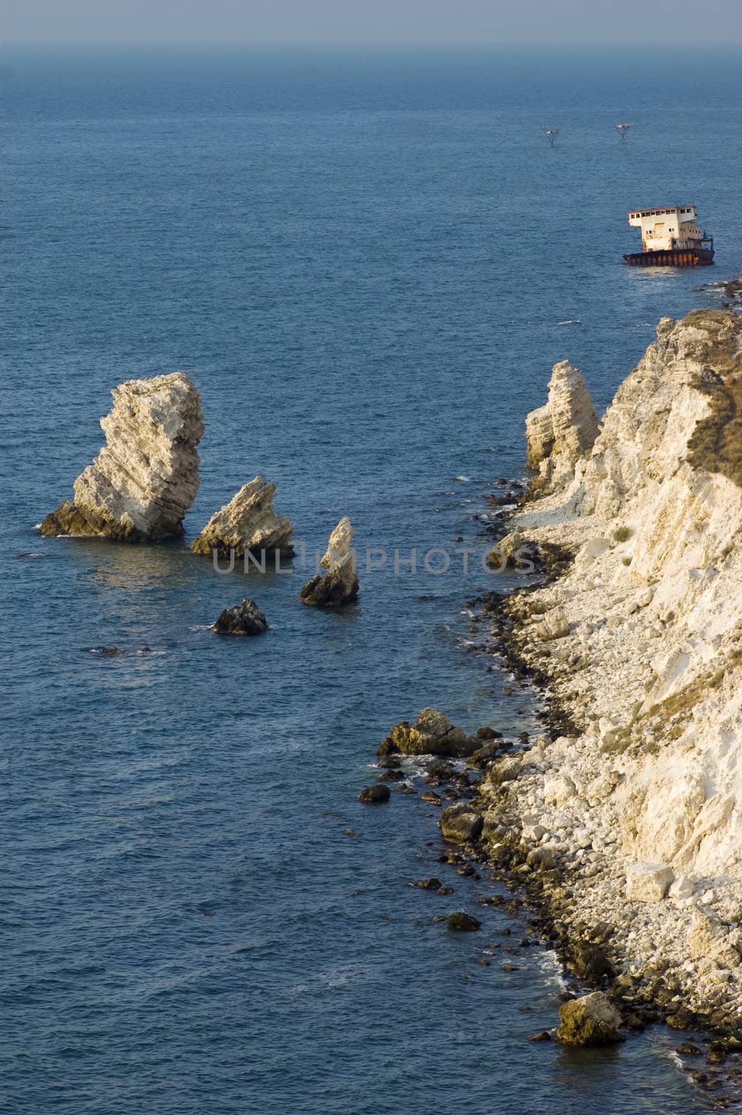 sunset time, sunken ship sitting on the bank near the rocky coastline