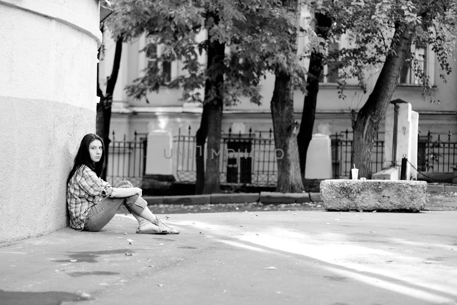 Girl sitting on asphalt near wall
