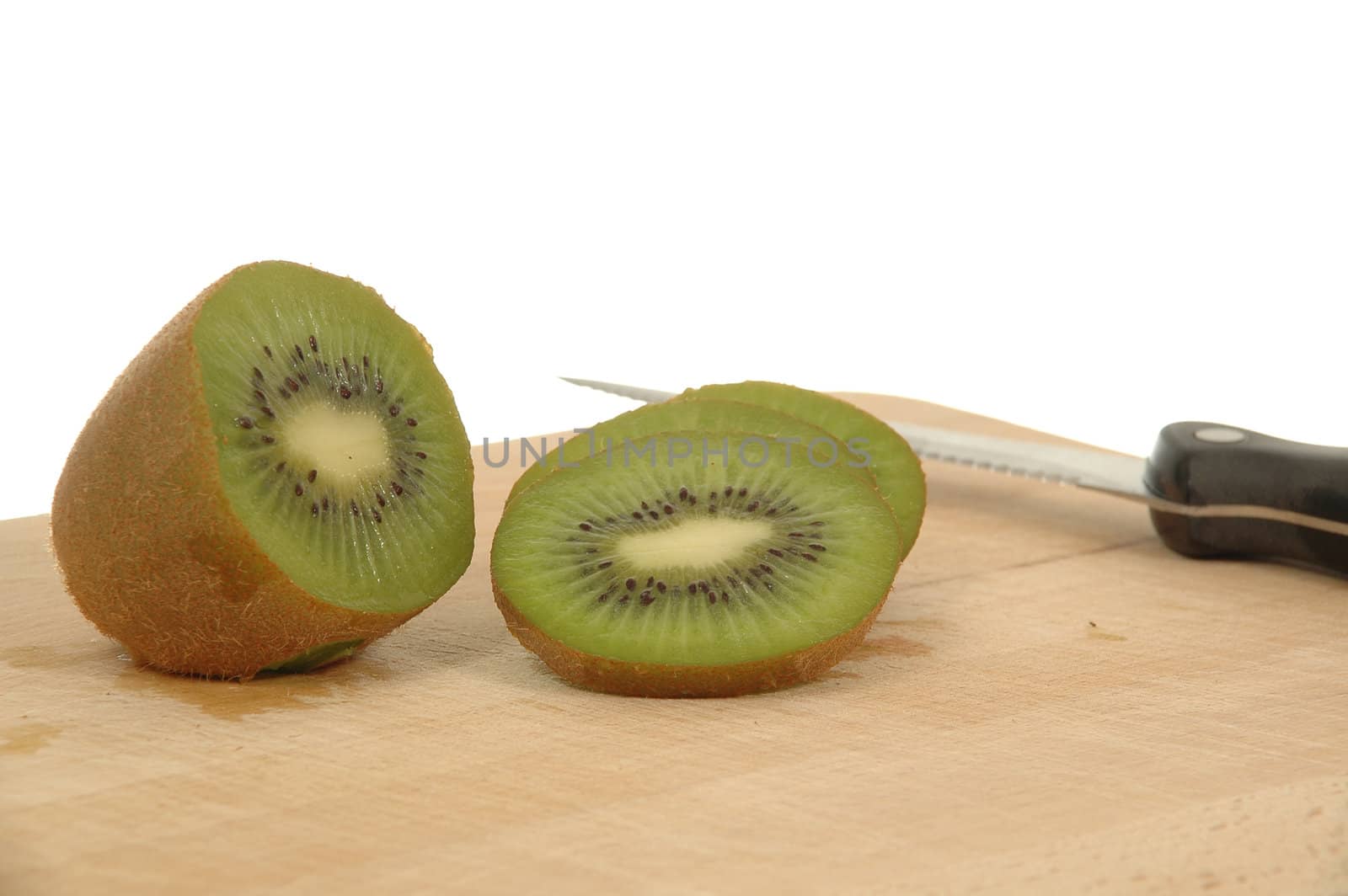 Half kiwi and slices is in focus. With knife and kiwies in the background.