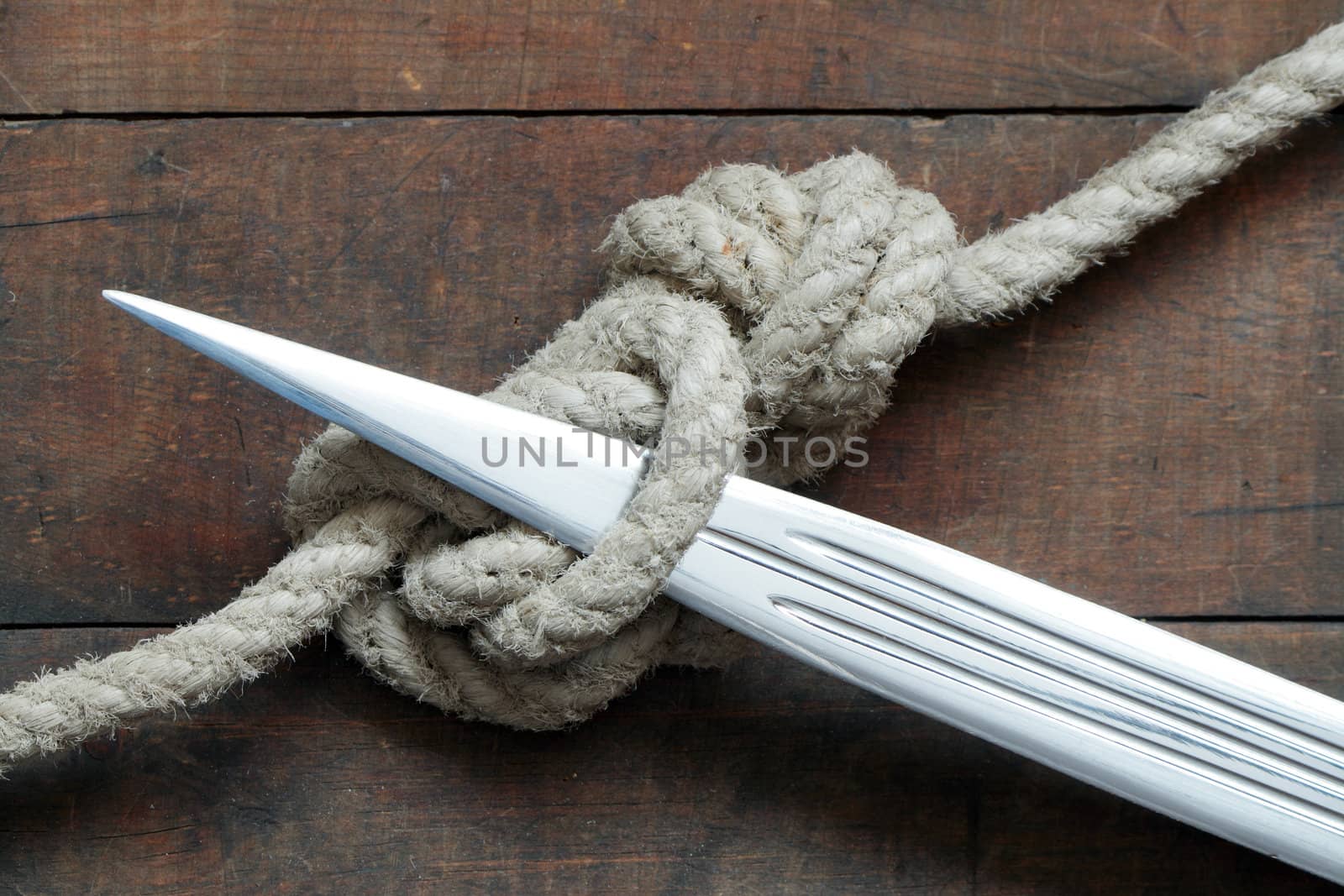 Closeup of dagger and rope tied knot on wooden background