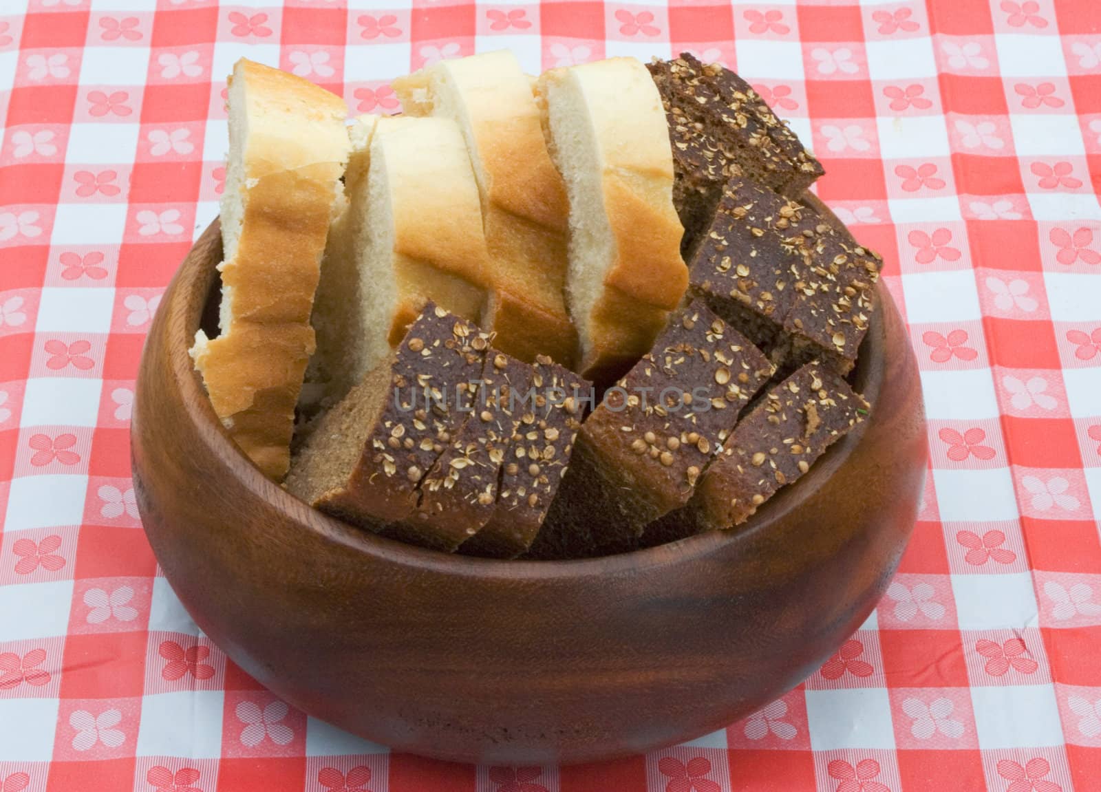 Slices of wheat and rye bread in a wooden bowl on a table covered with checkered buckram