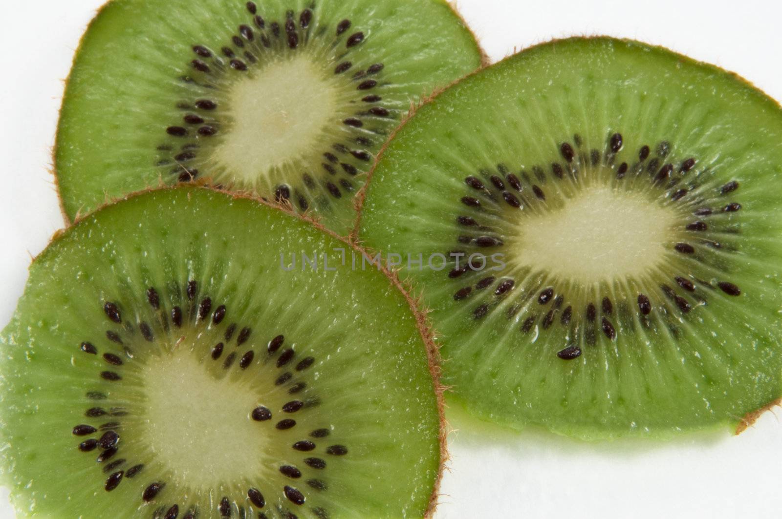 Close up of three kiwifruit slices arranged over white.
