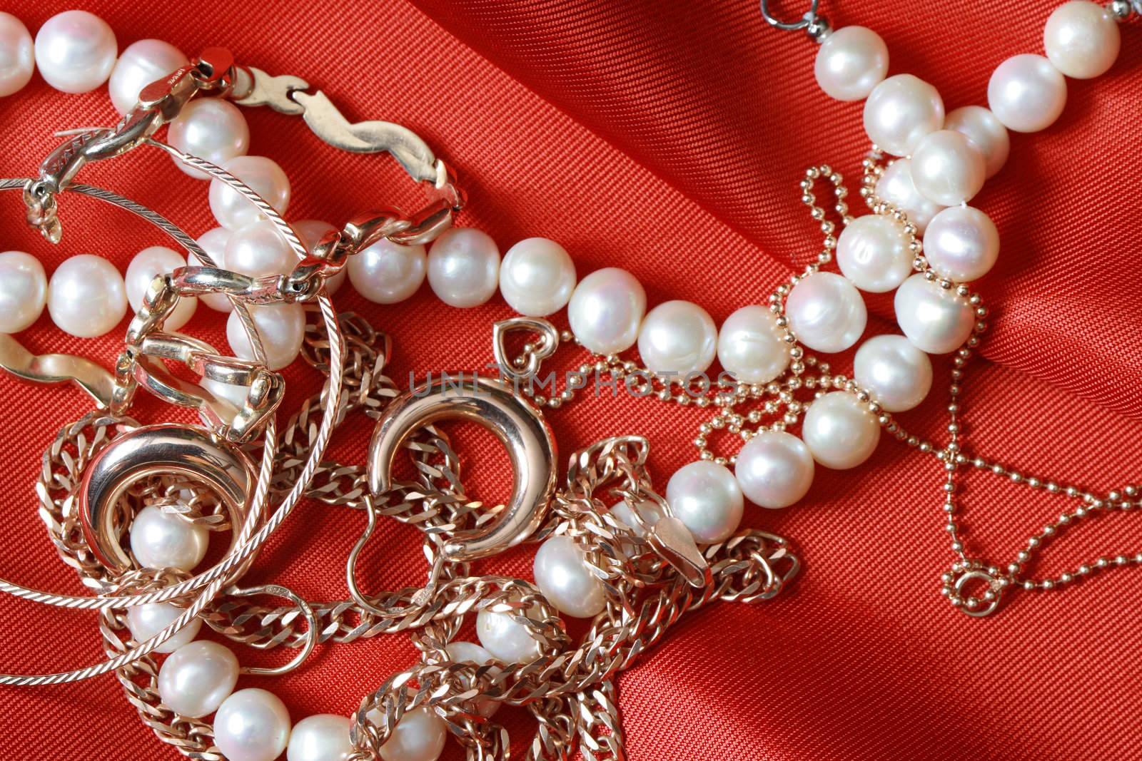 Pearl necklace and gold jewelry lying on red silk background with copy space