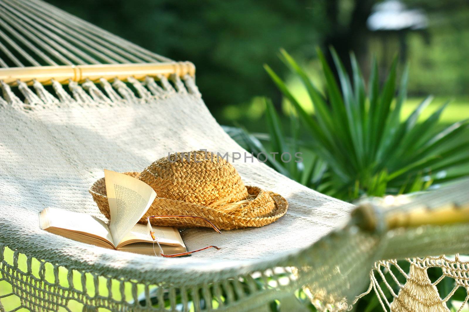 Hammock, book, hat, and glasses on a sunny summer day