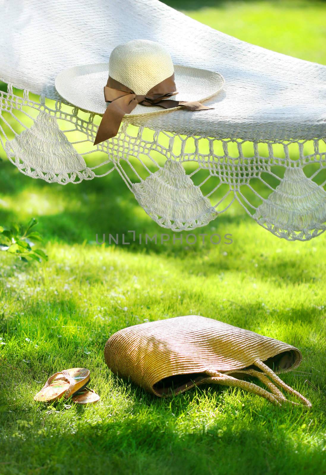 Straw hat with brown ribbon laying on hammock by Sandralise