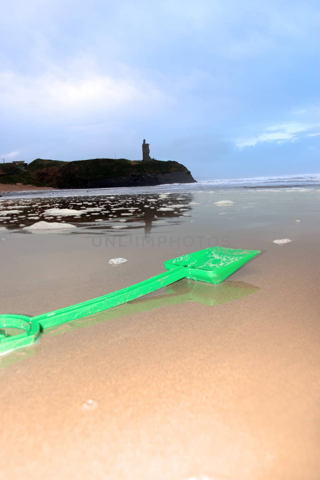 green plastic spade lying on a beach in ireland with ballybunion castle in background as if building a sand castle