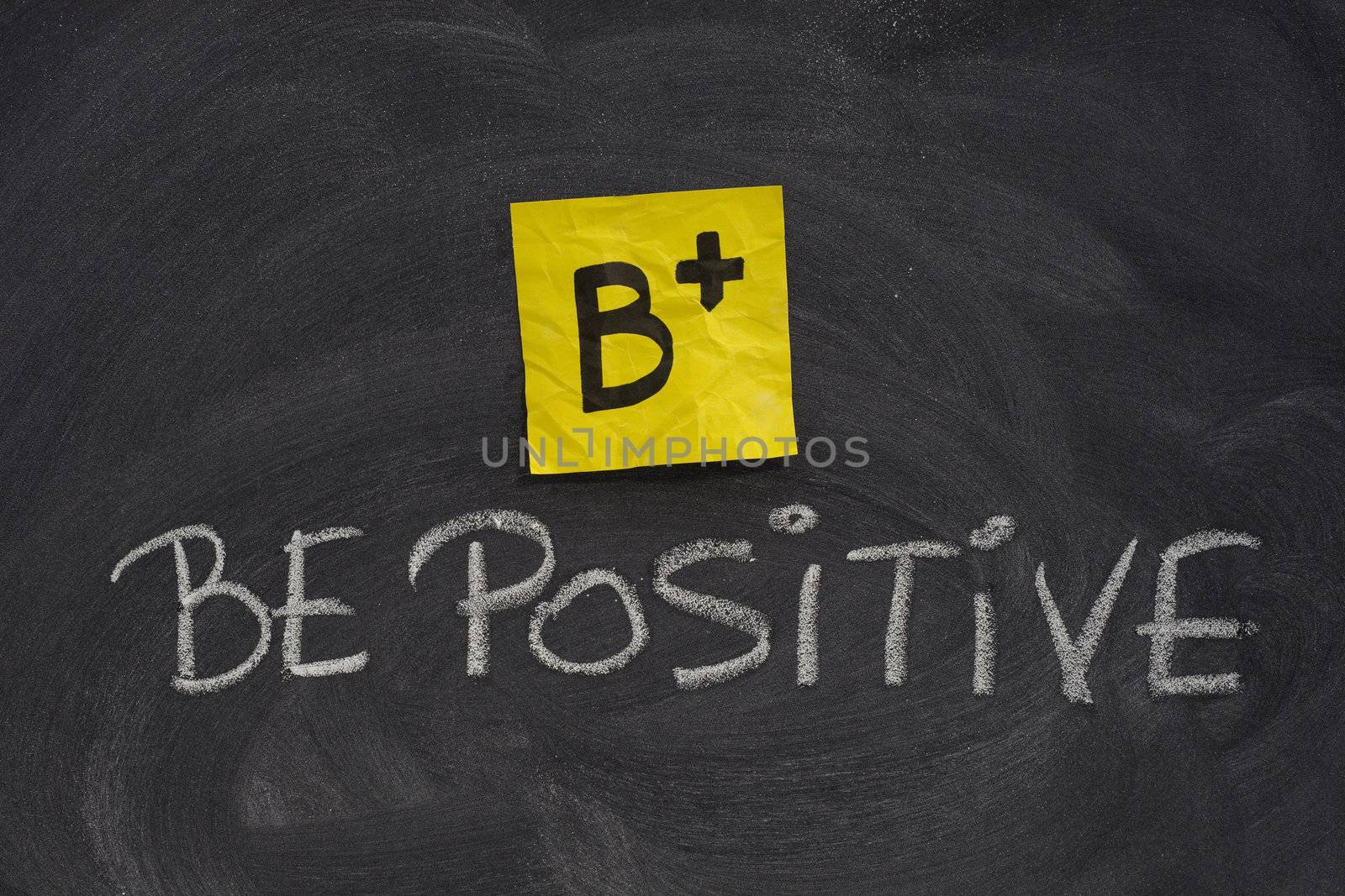 B+, be positive concept, yellow sticky note and white chalk handwriting on blackboard