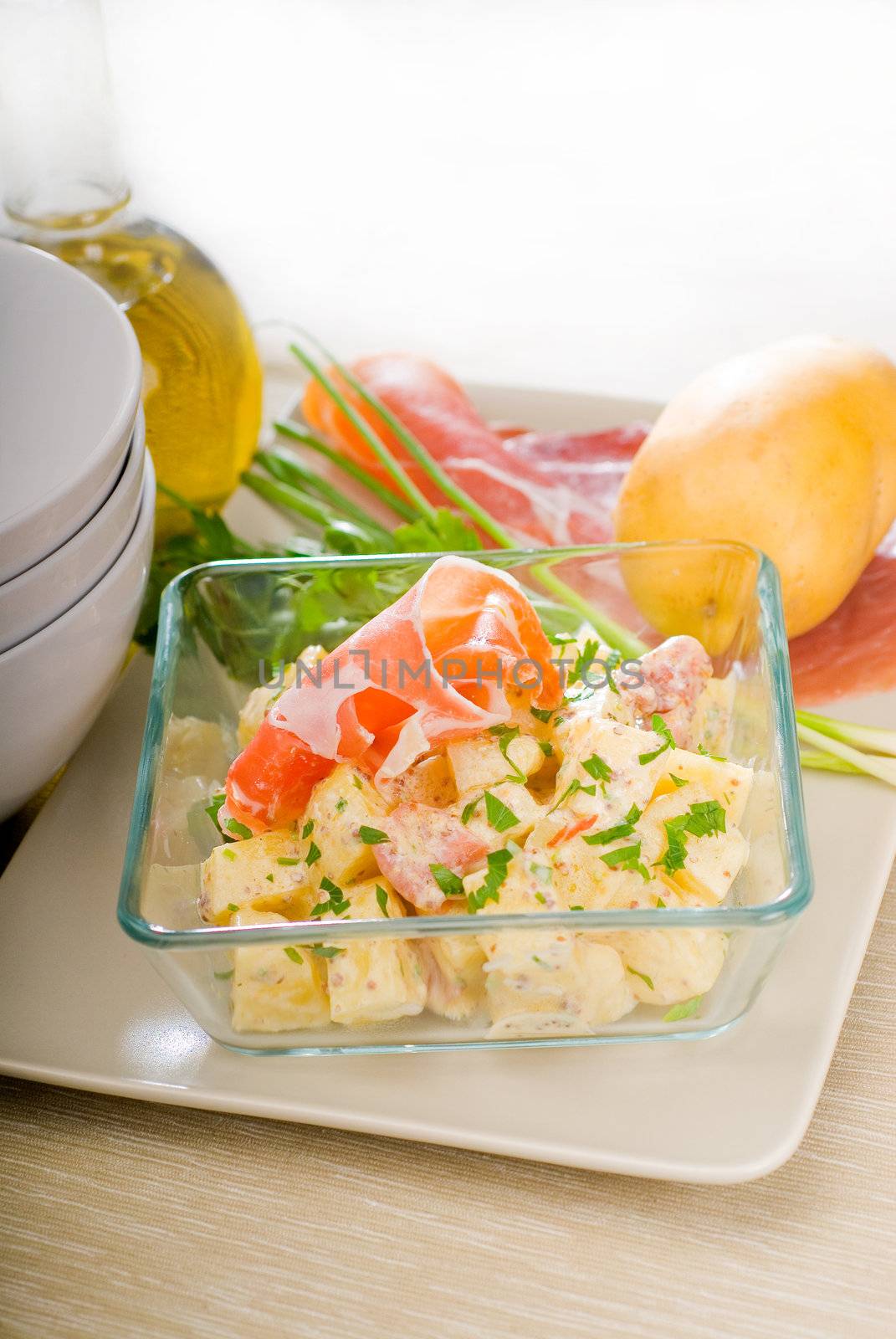 fresh home made parma ham and potato salad,with raw ingredients around with bowls and dishware on a table