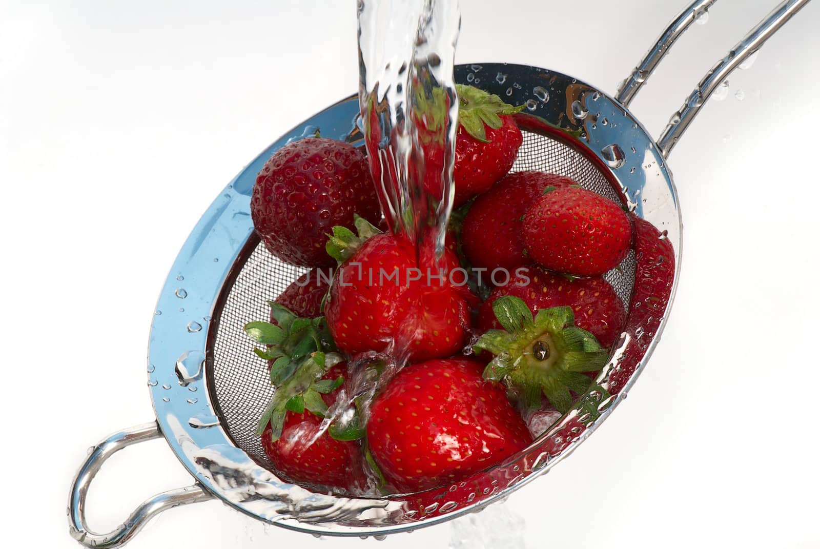 Ripe strawberry in a colander under a jet of pure water.