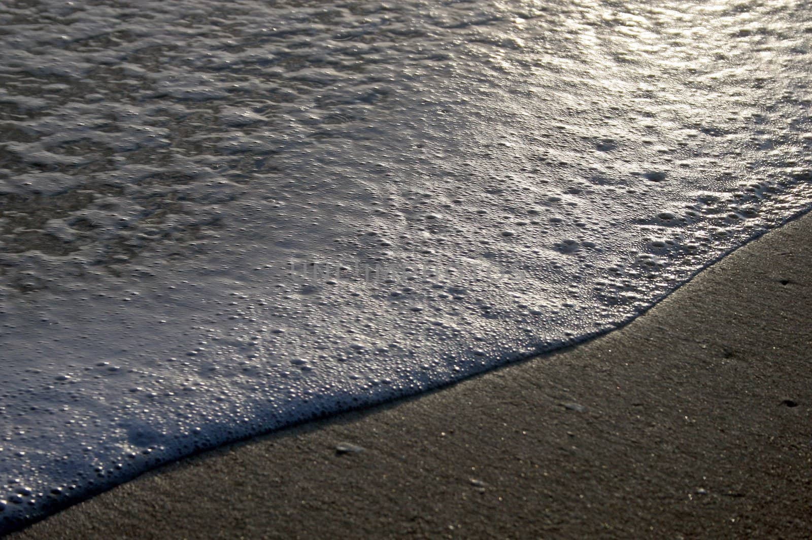 Waves coming ashore, at sunset, beach and foam.