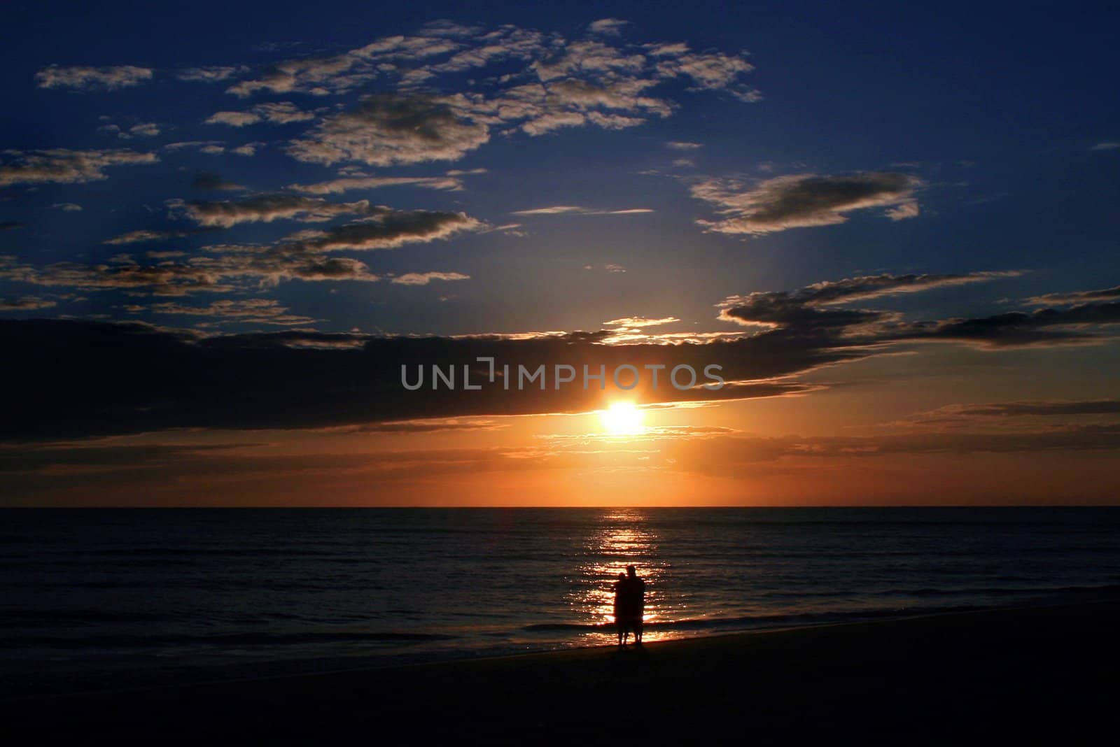 A couple standing watching the beautiful sunset.