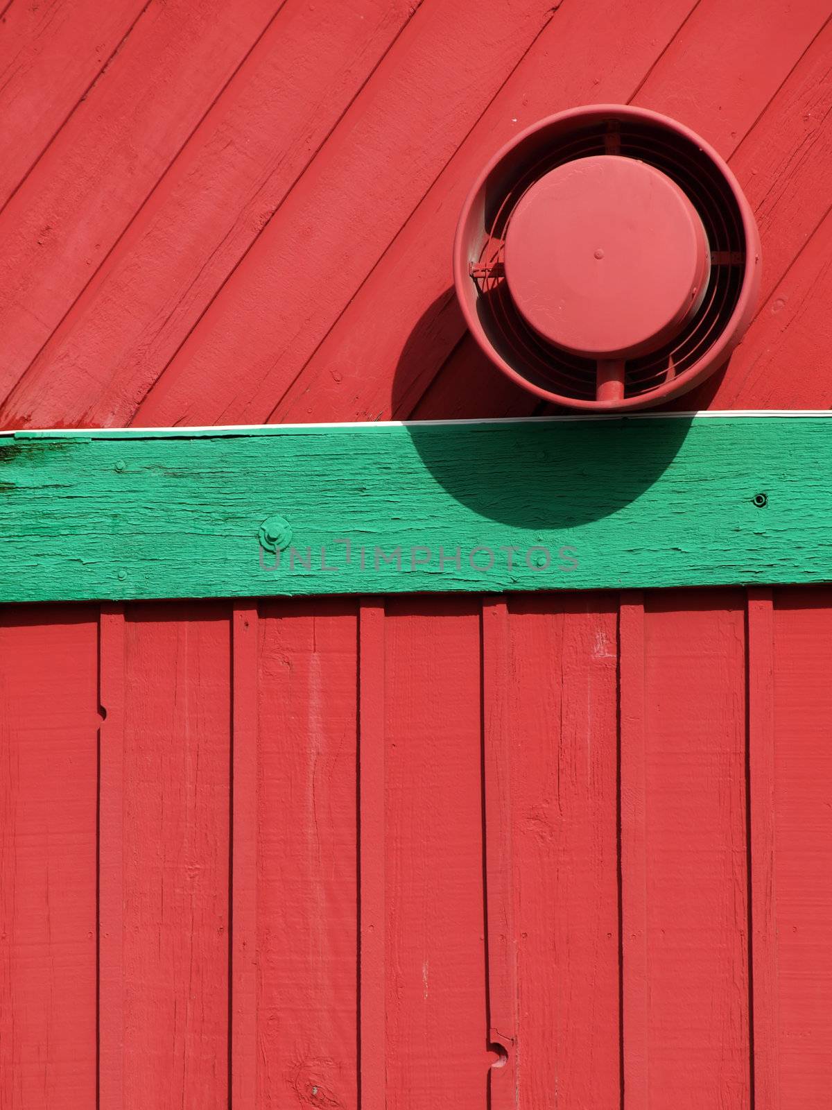 A red wood sided building with green painted trim. Exterior shot showing an exhaust fan.