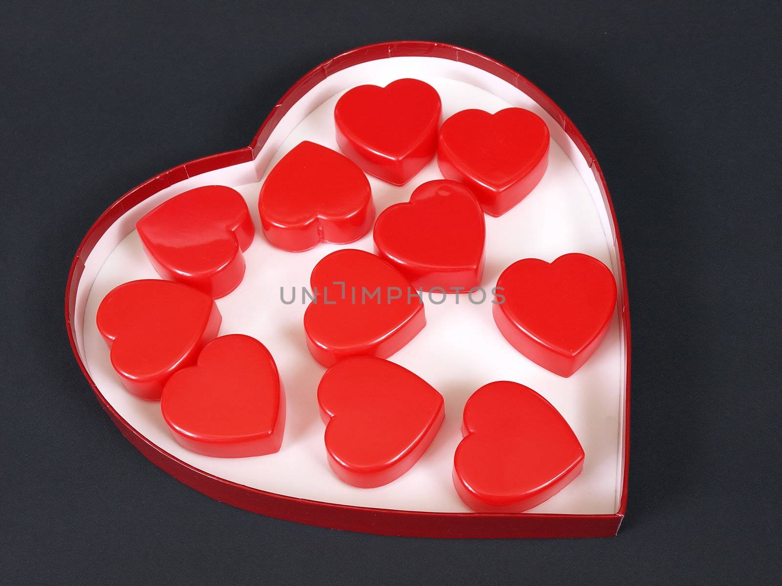 A heart shaped box filled with red heart shapes over a black background.