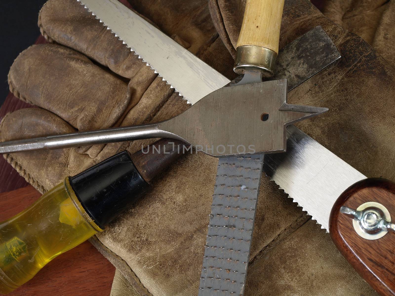 Woodworking tools and a pair of dirty worn gloves over a wood grain background.