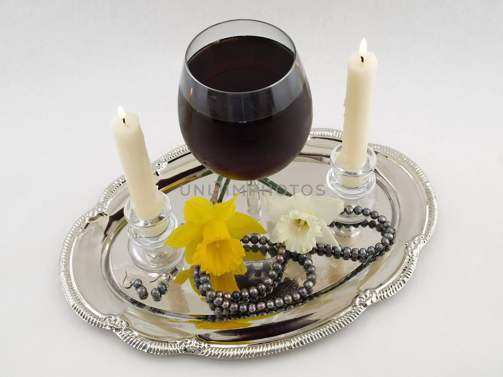 White candles, red wine, flowers and pearls on a silver tray isolated on a white background