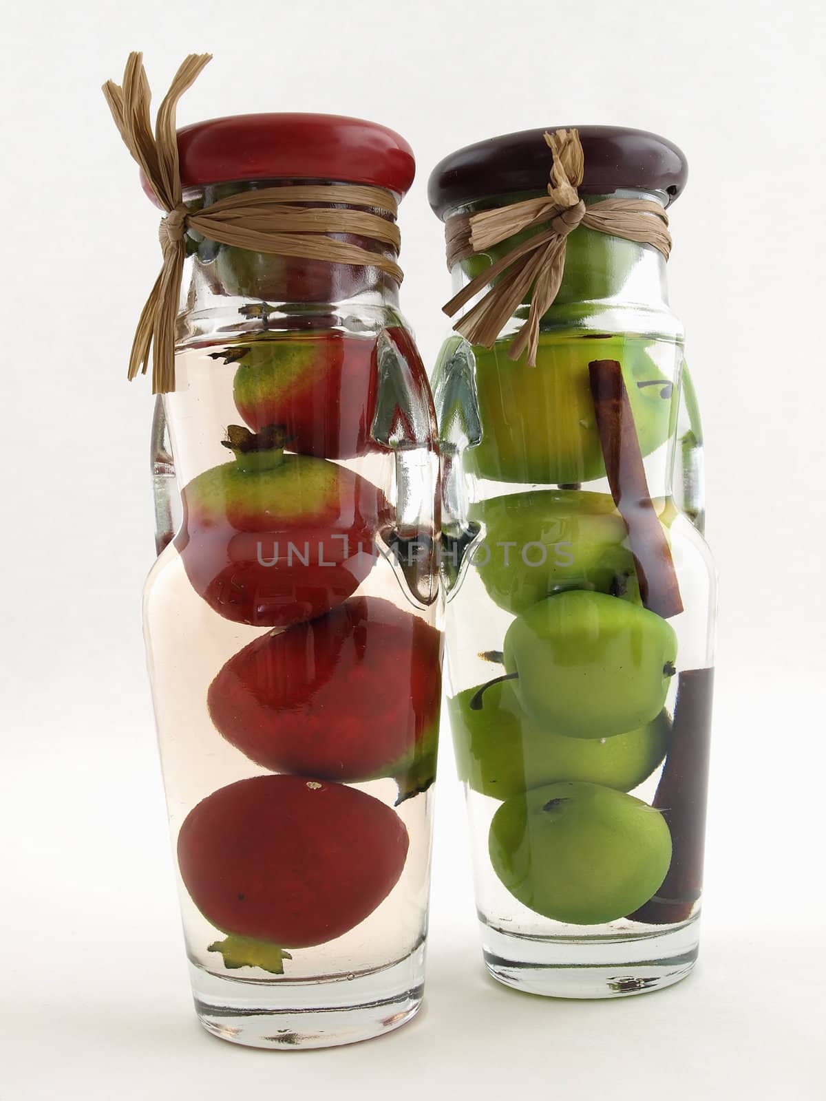 Glass jars filled with green apples and red pomegranates, on a white background.