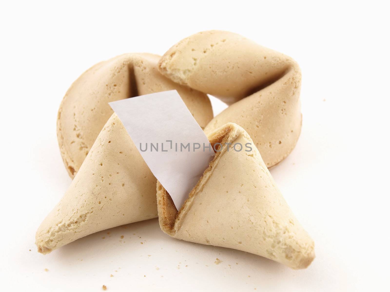 A broken fortune cookie with whole cookies over a white background. Cookie has blank fortune sticking out of one side.