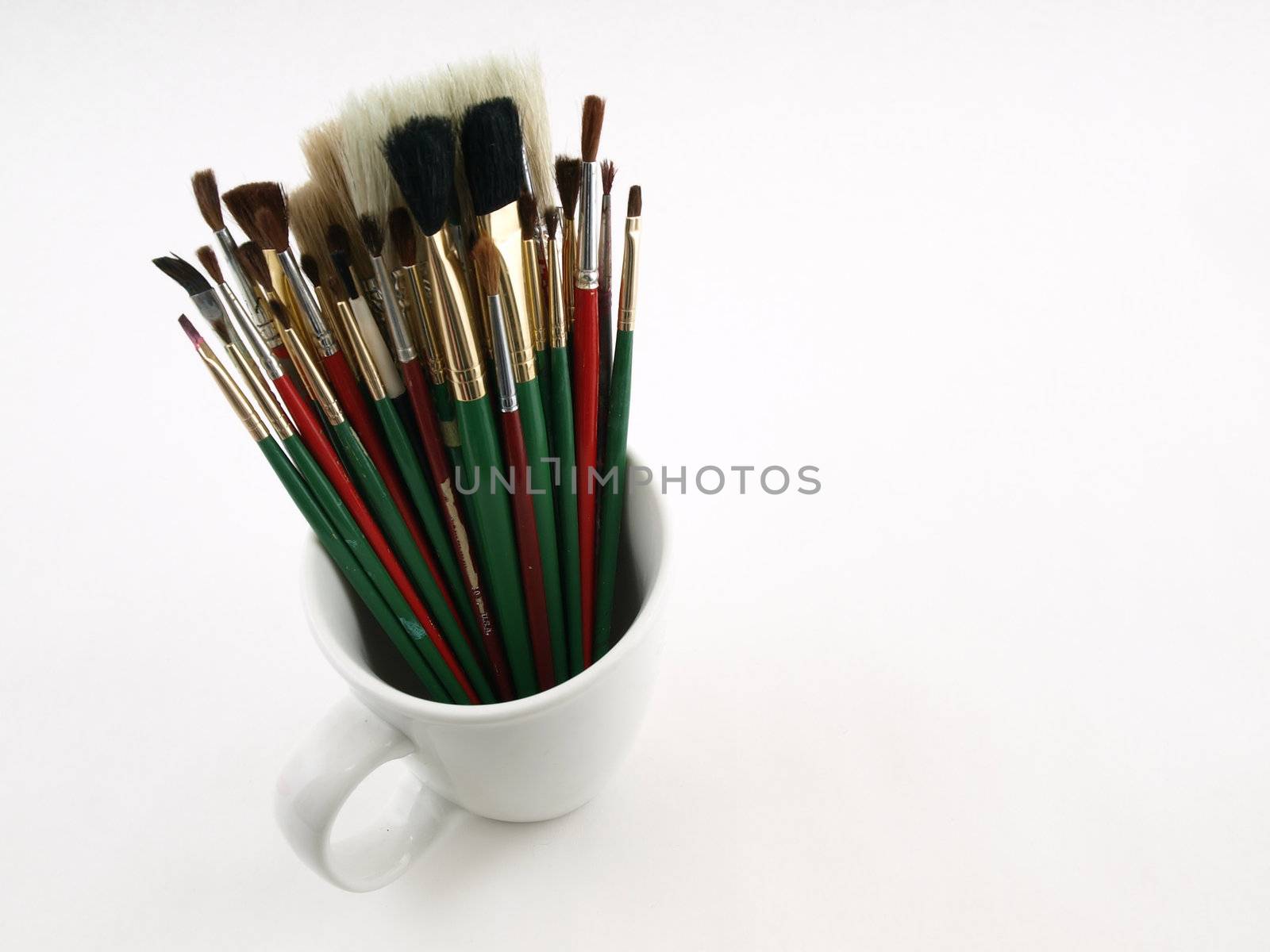 A white cup holds a group of artist brushes over a white background.