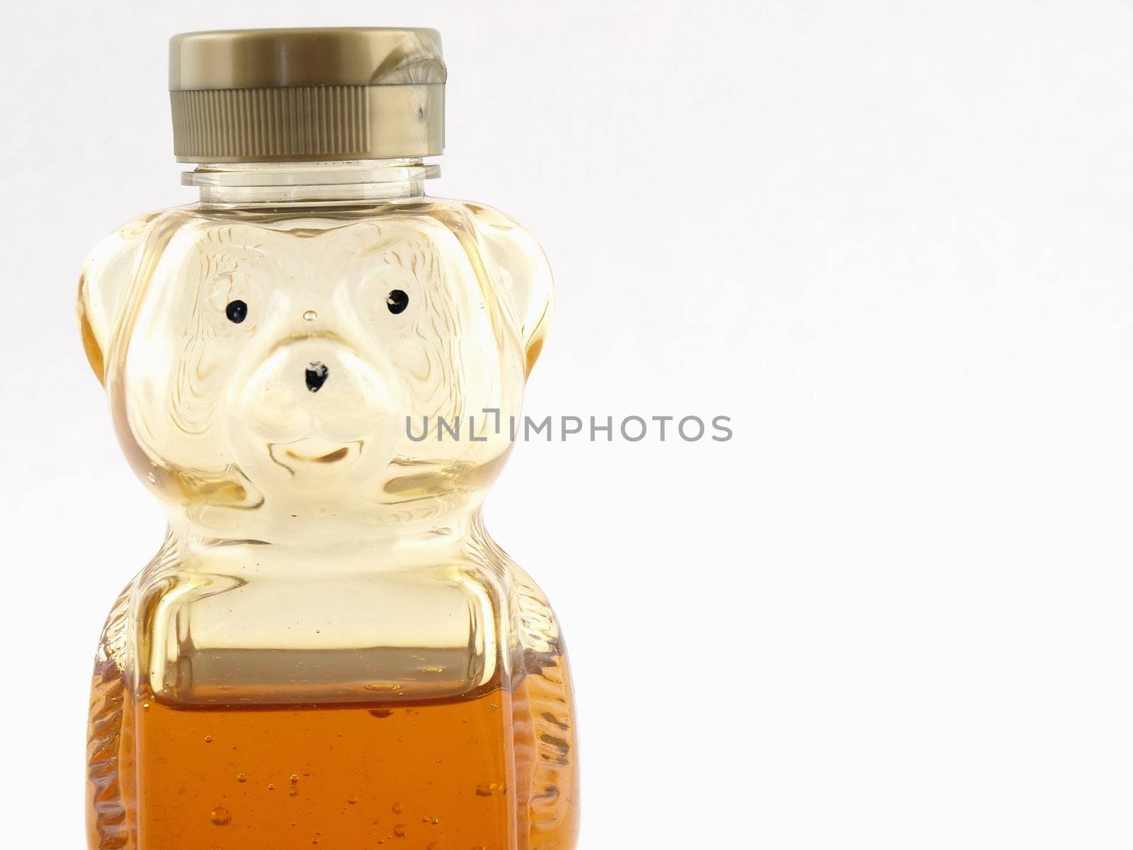 A plastic bear shaped container half full of honey over a white background. Offset with room for text.