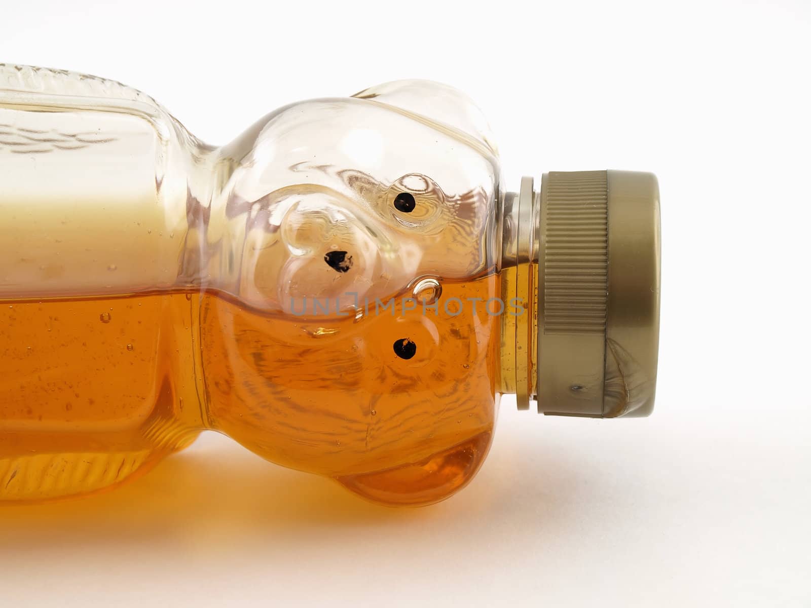 A plastic bear shaped container half full of honey tipped on its side over a white background.