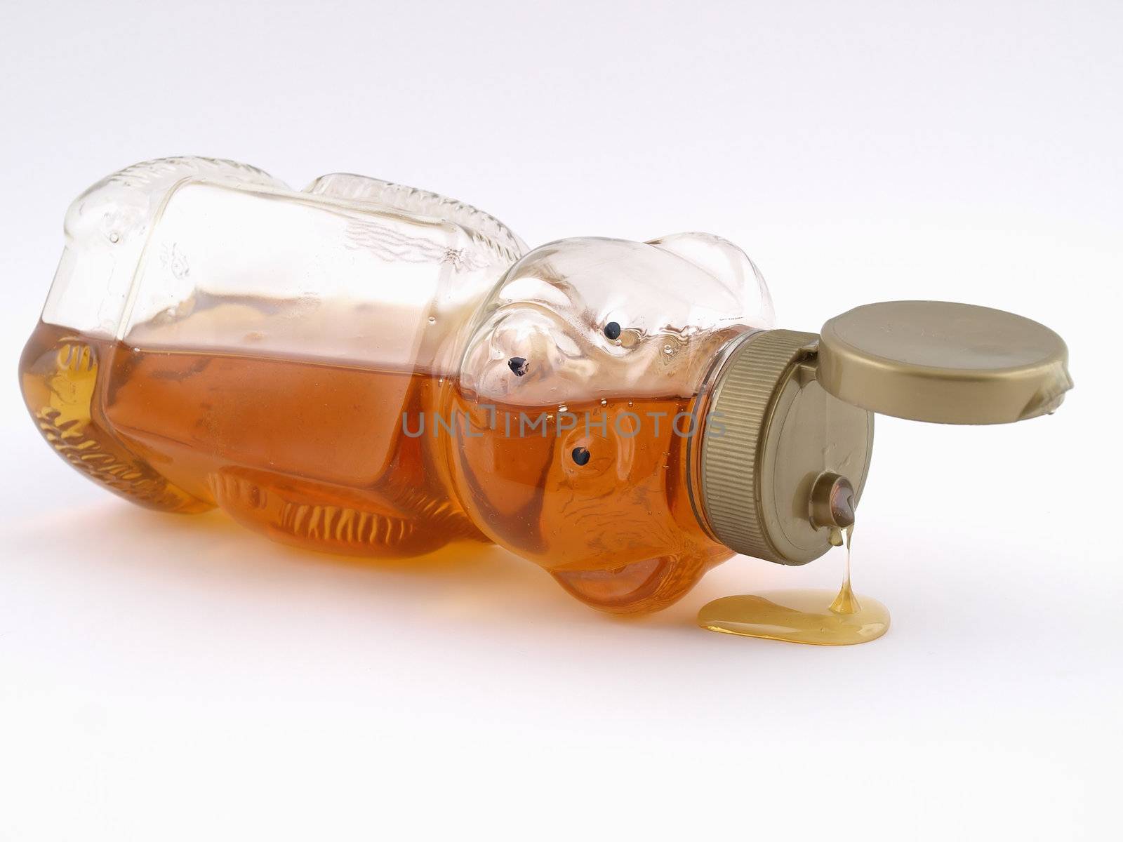 A plastic bear shaped container full of honey on it's side, cap open and dripping.