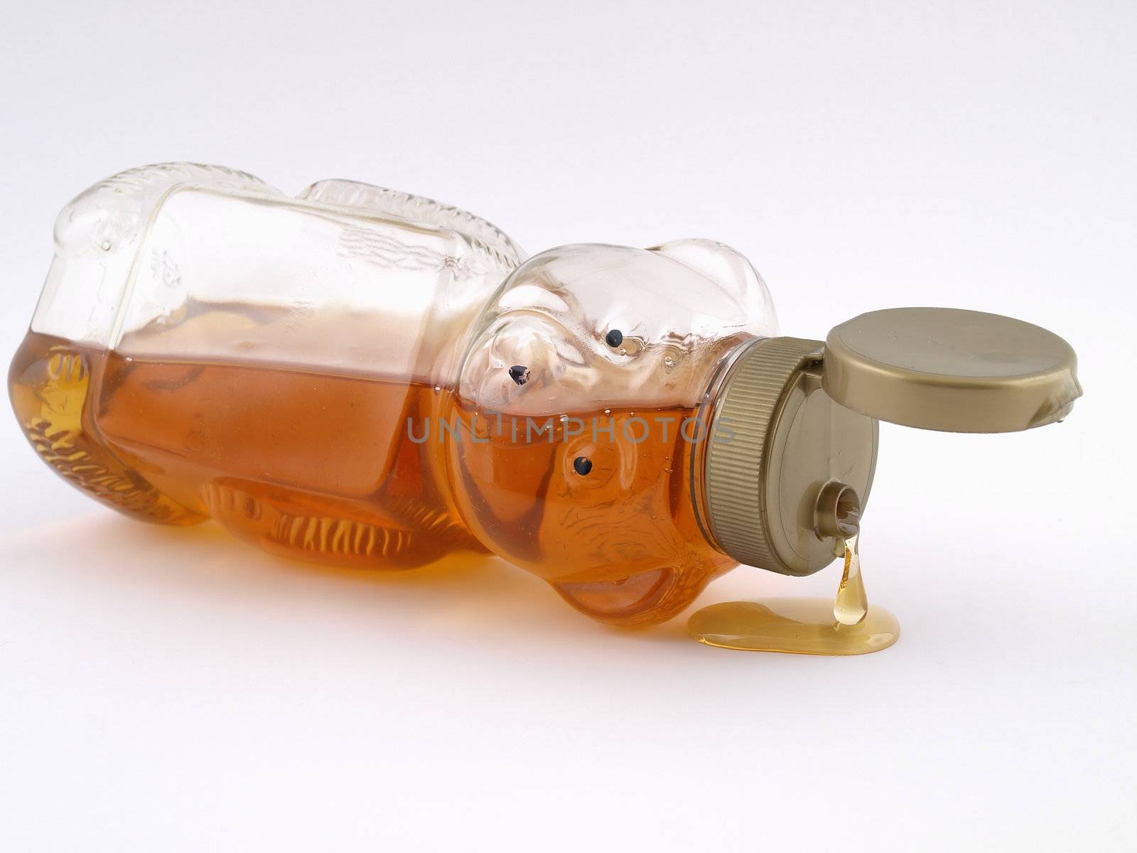 A plastic bear shaped container full of honey on it's side, cap open and dripping.