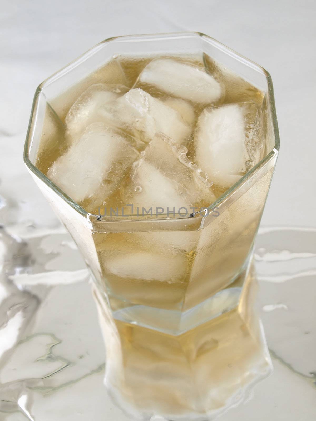 A glass of Alcohol with ice floating in a glass isolated on a  reflective surface