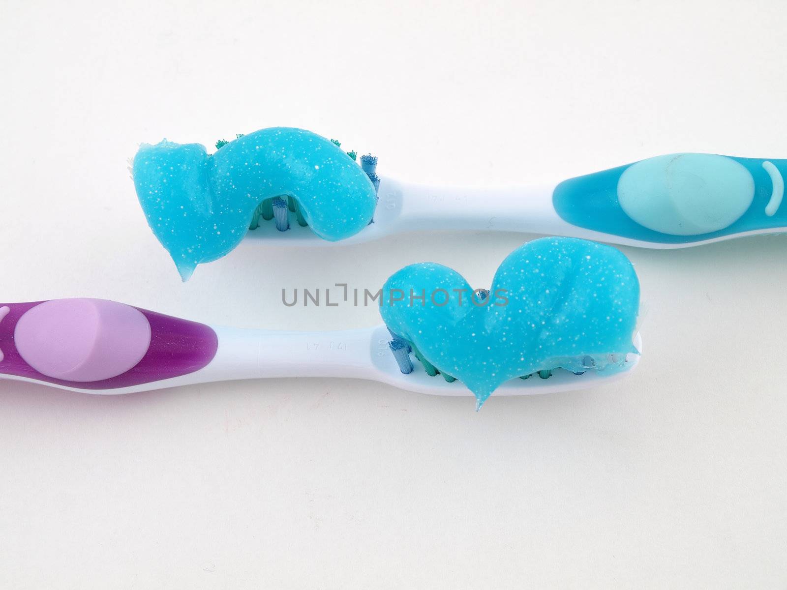 Two toothbrushes with a blue gel toothpaste over a white background.