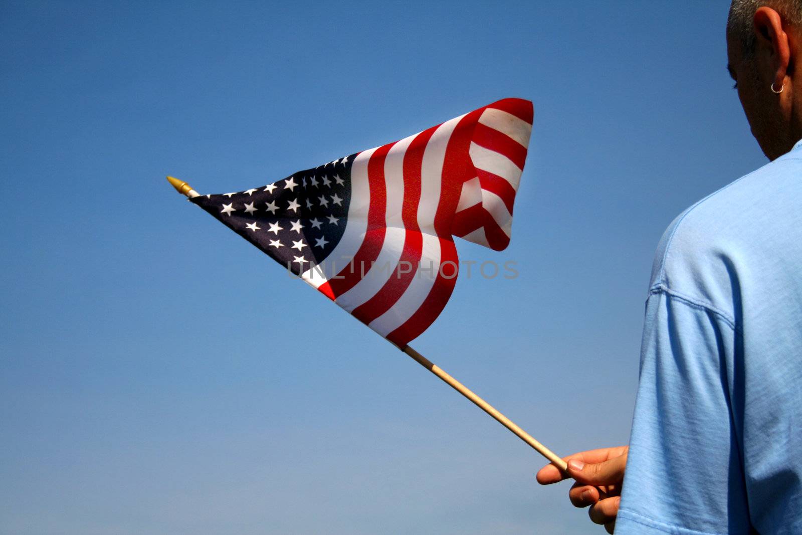 Person holding the American flag outside with a beautiful blue sky as the background.