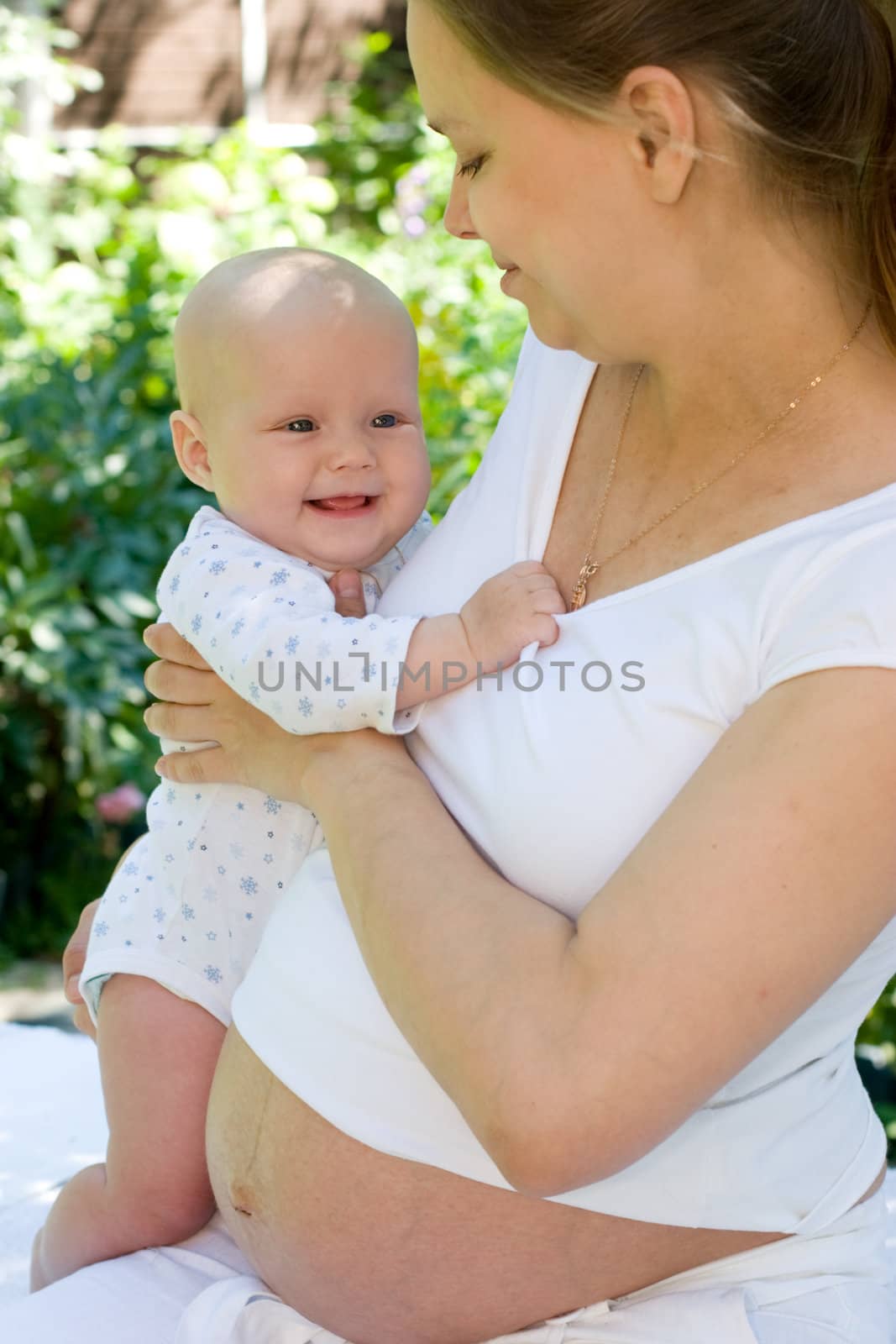 Young pregnant woman holding baby girl at summer garden