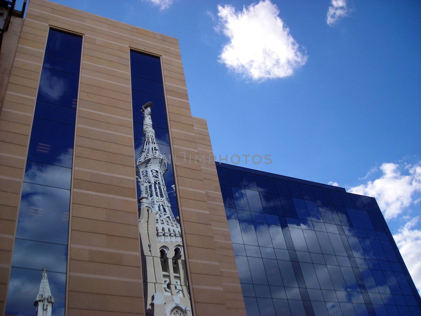 Reflection of a church tower on an office building on a sunny afternoon in Madrid.