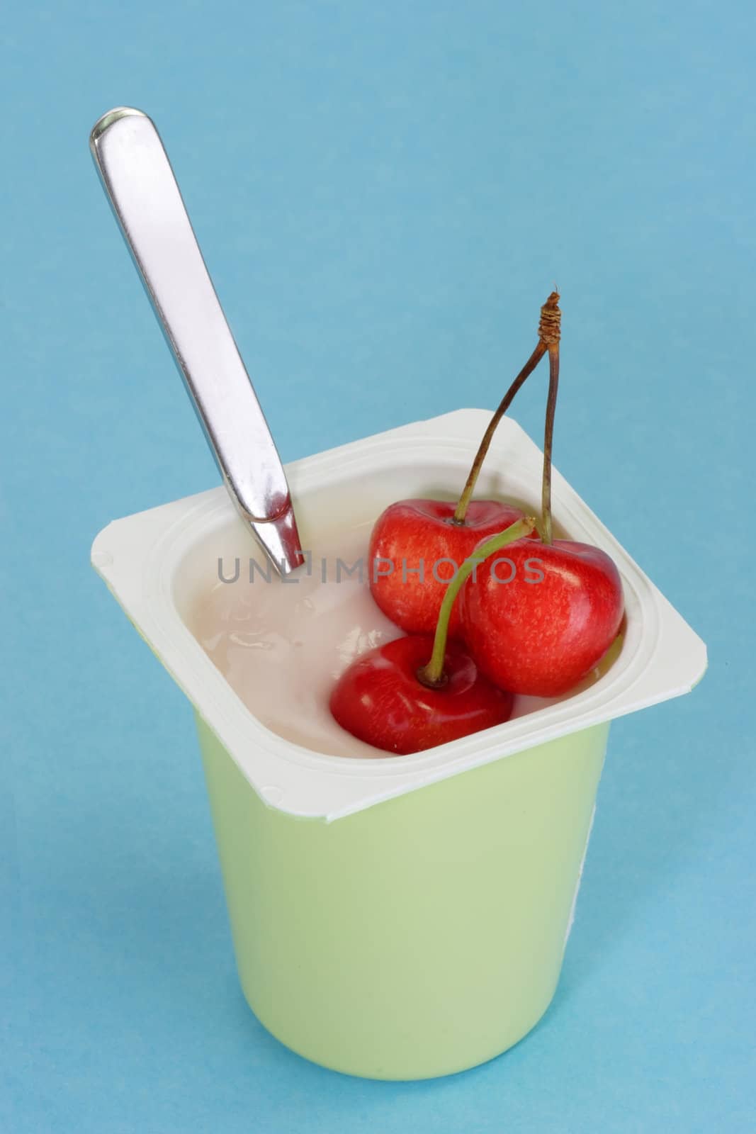 Cup of yoghourt with fresh cherries on light blue background