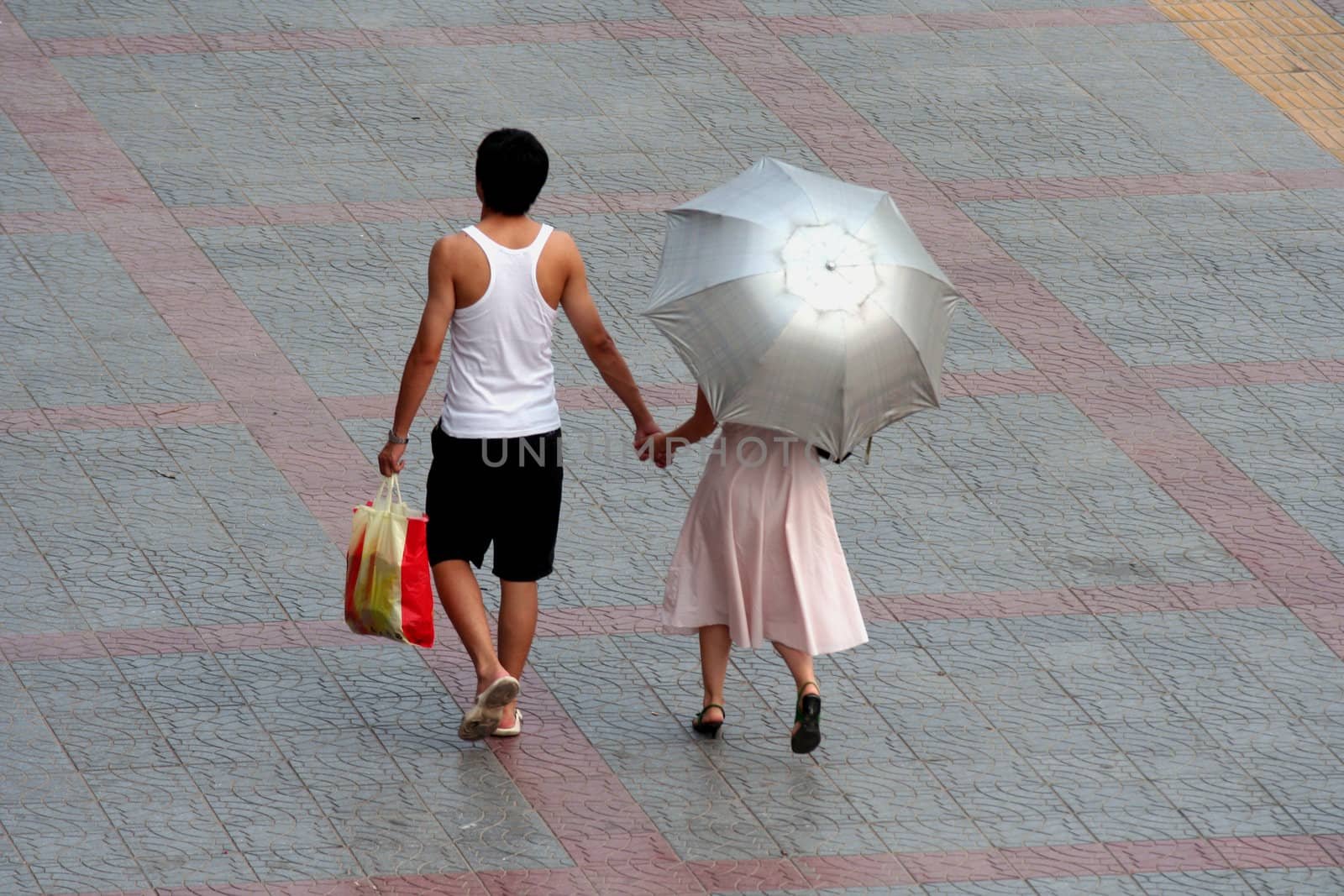 Young adult man and woman walking together in the street. The umbrella of the woman contrast with the clothes of the man but it is because the umbrella protect against the sun. Typical street scene in China. I take this picture in Xi'an.