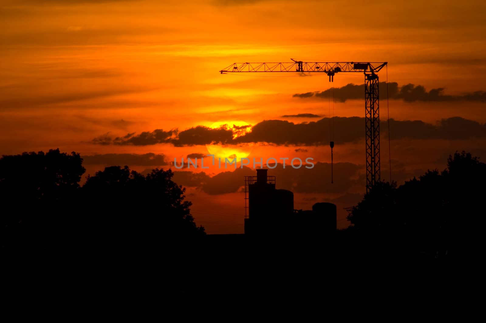 sunset with a silhouette of a crane and factory in the back