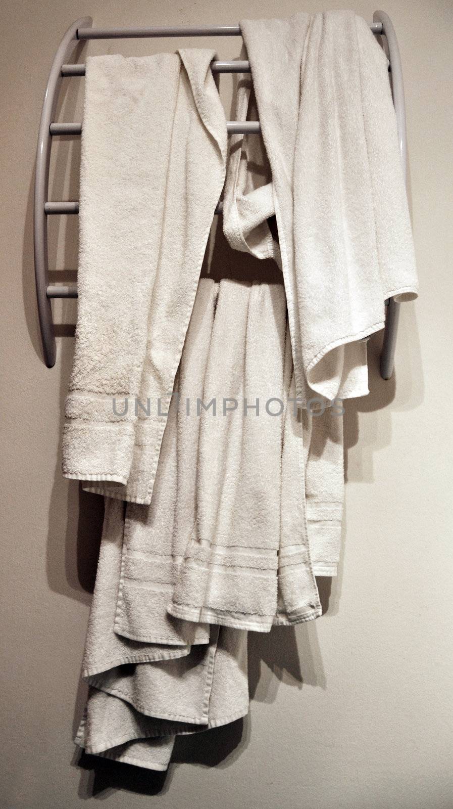 Several used hotel washroom towels on modern white rack in front of white wall