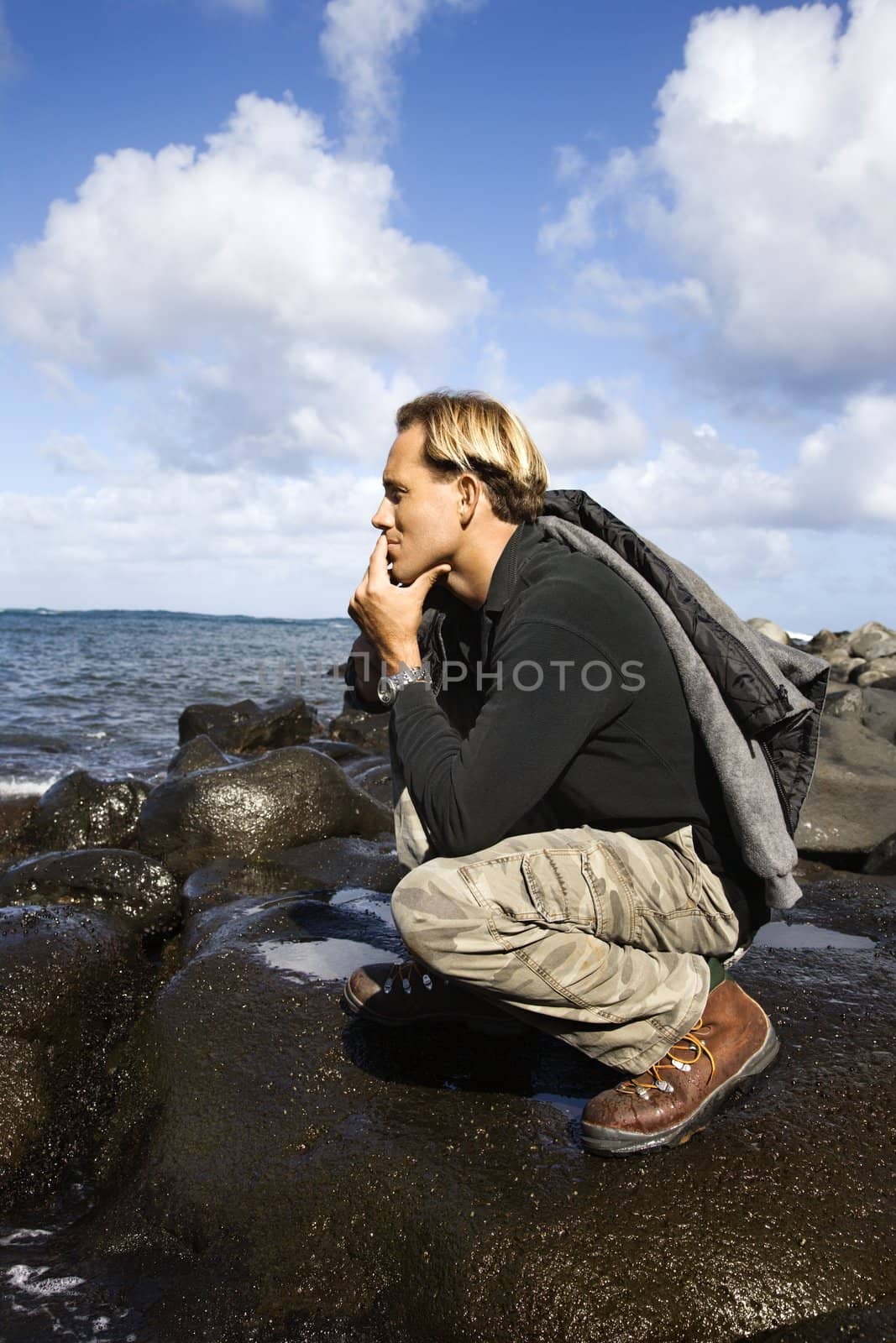 Man kneeling at beach. by iofoto