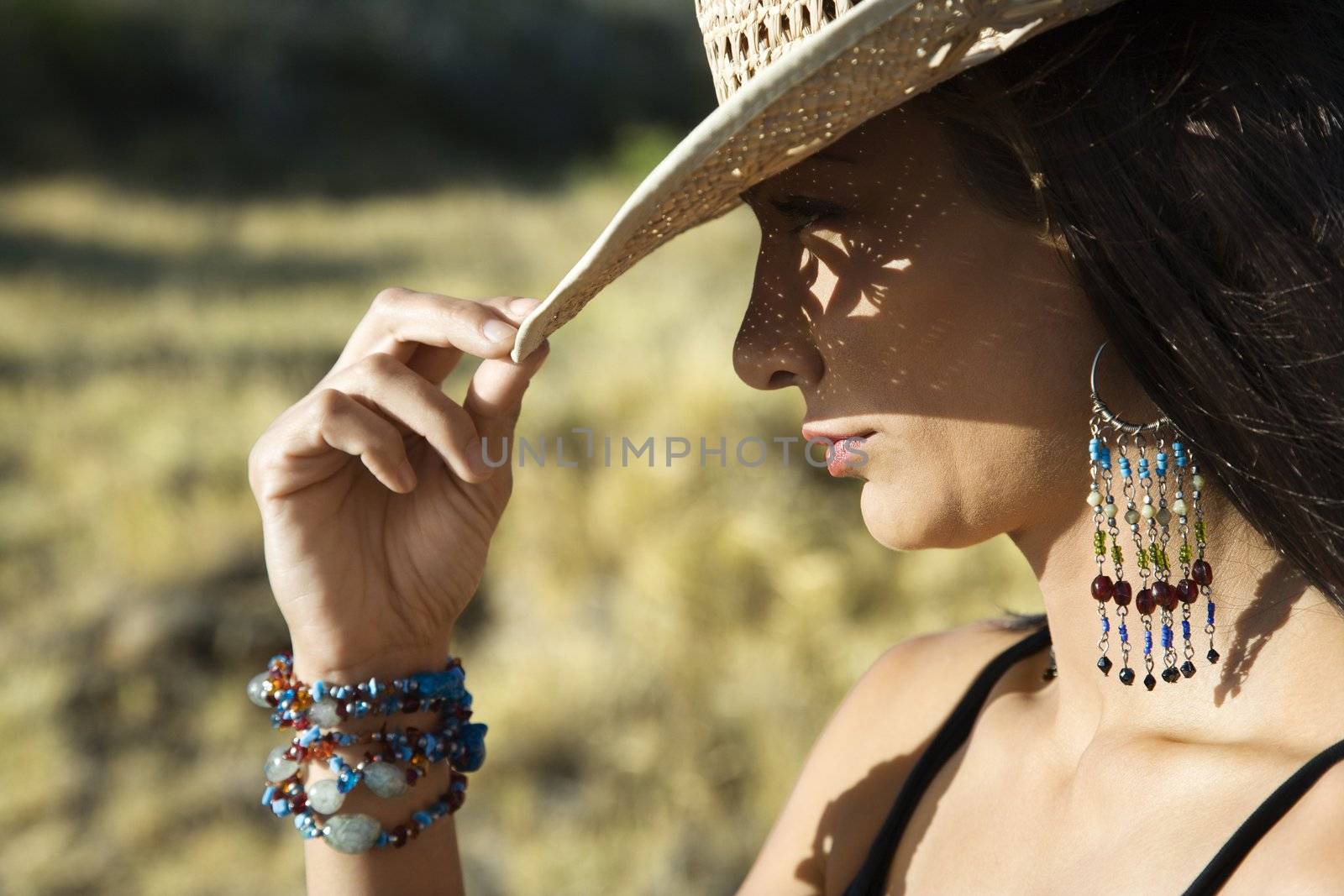 Close-up profile of mid-adult Caucasian woman tipping straw cowboy hat.