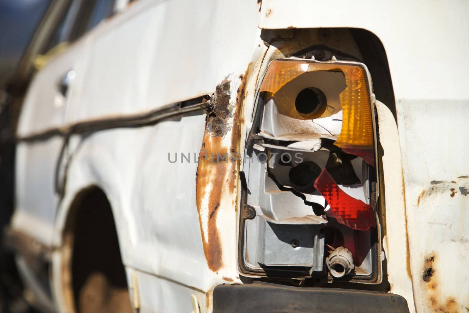 Close-up of busted taillight on rear end of old abandoned and rusted car .