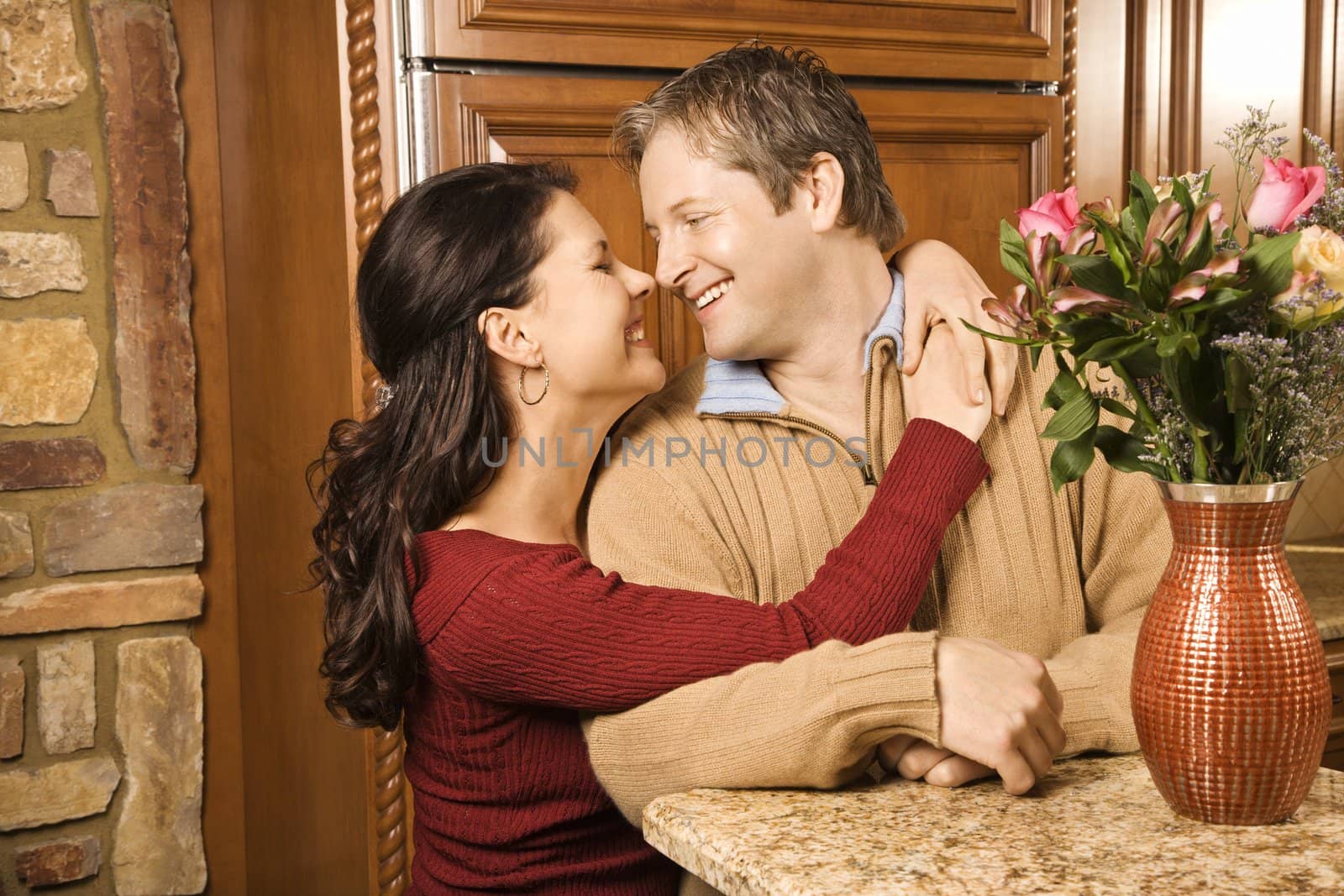 Caucasian woman with arms around Caucasian man smiling at each other in kitchen.
