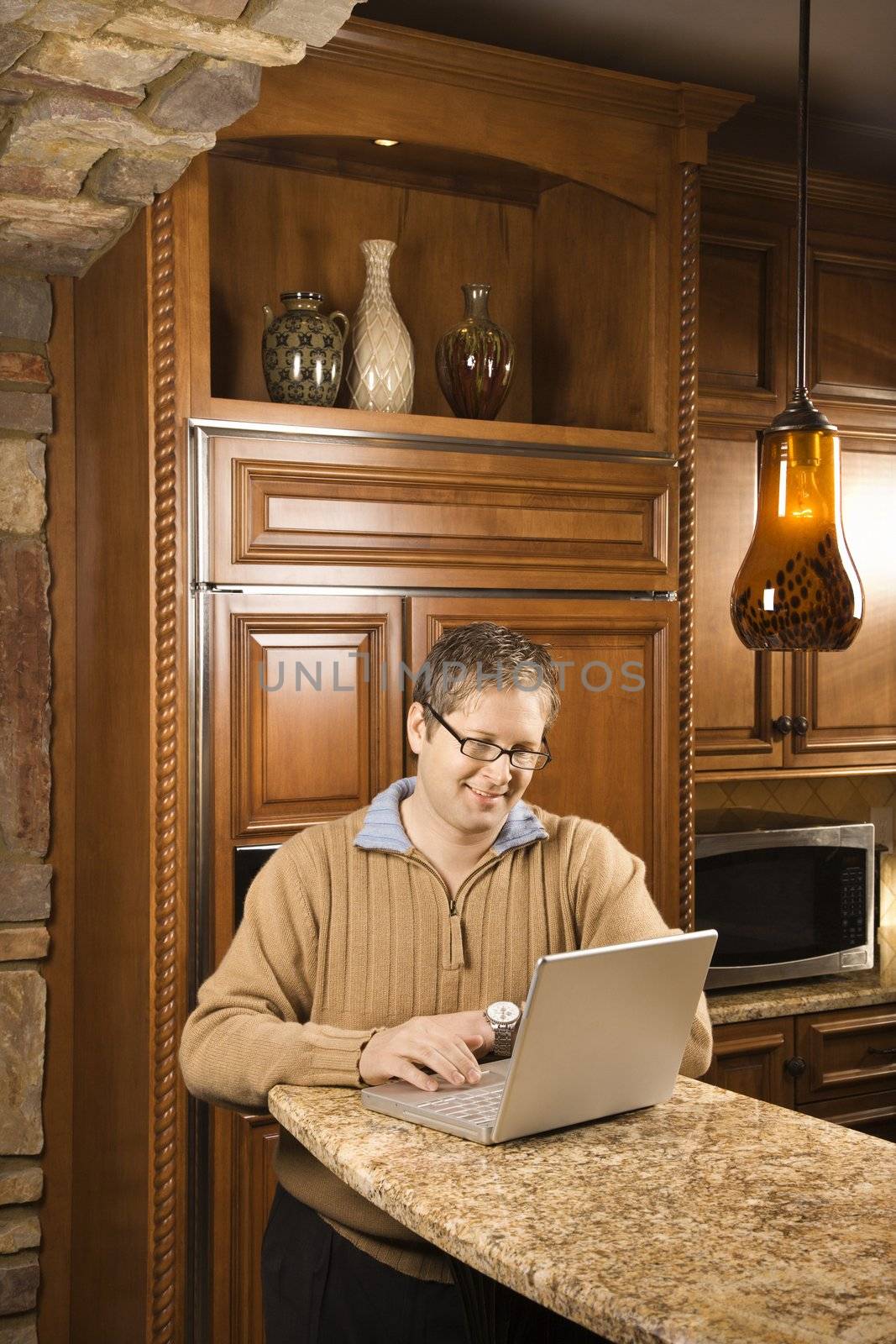 Caucasian man working on laptop computer in kitchen.