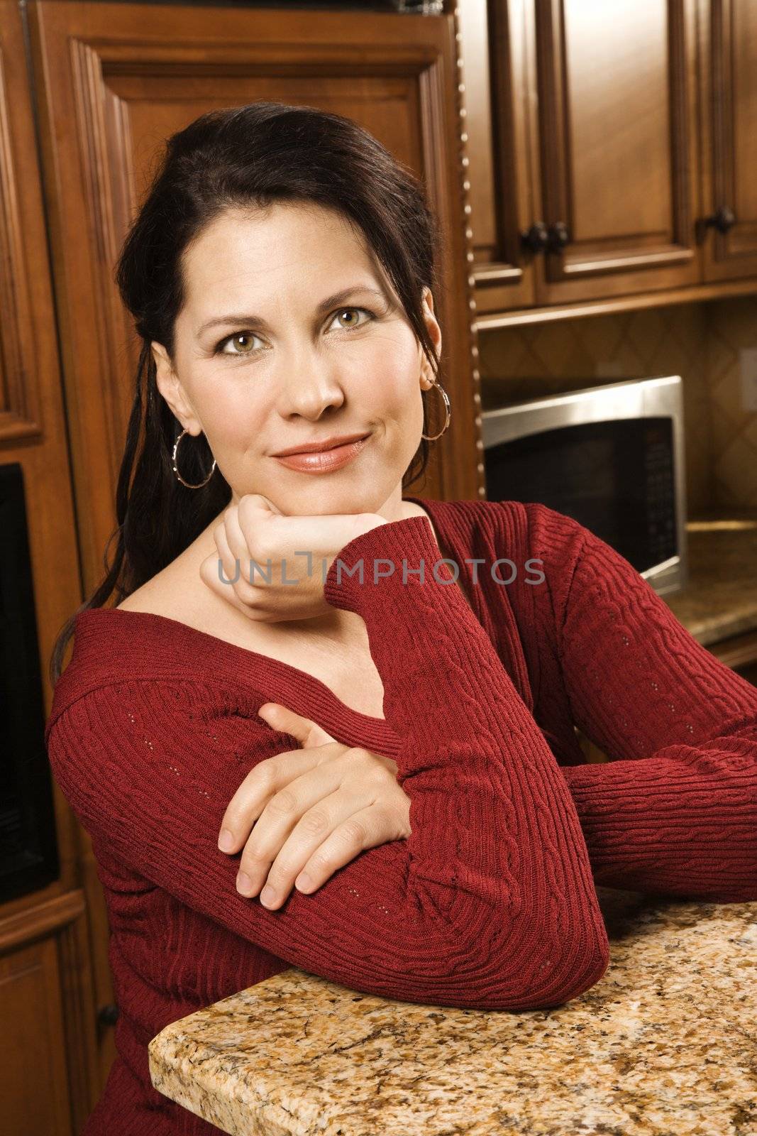 Caucasian woman leaning on kitchen counter looking at viewer.
