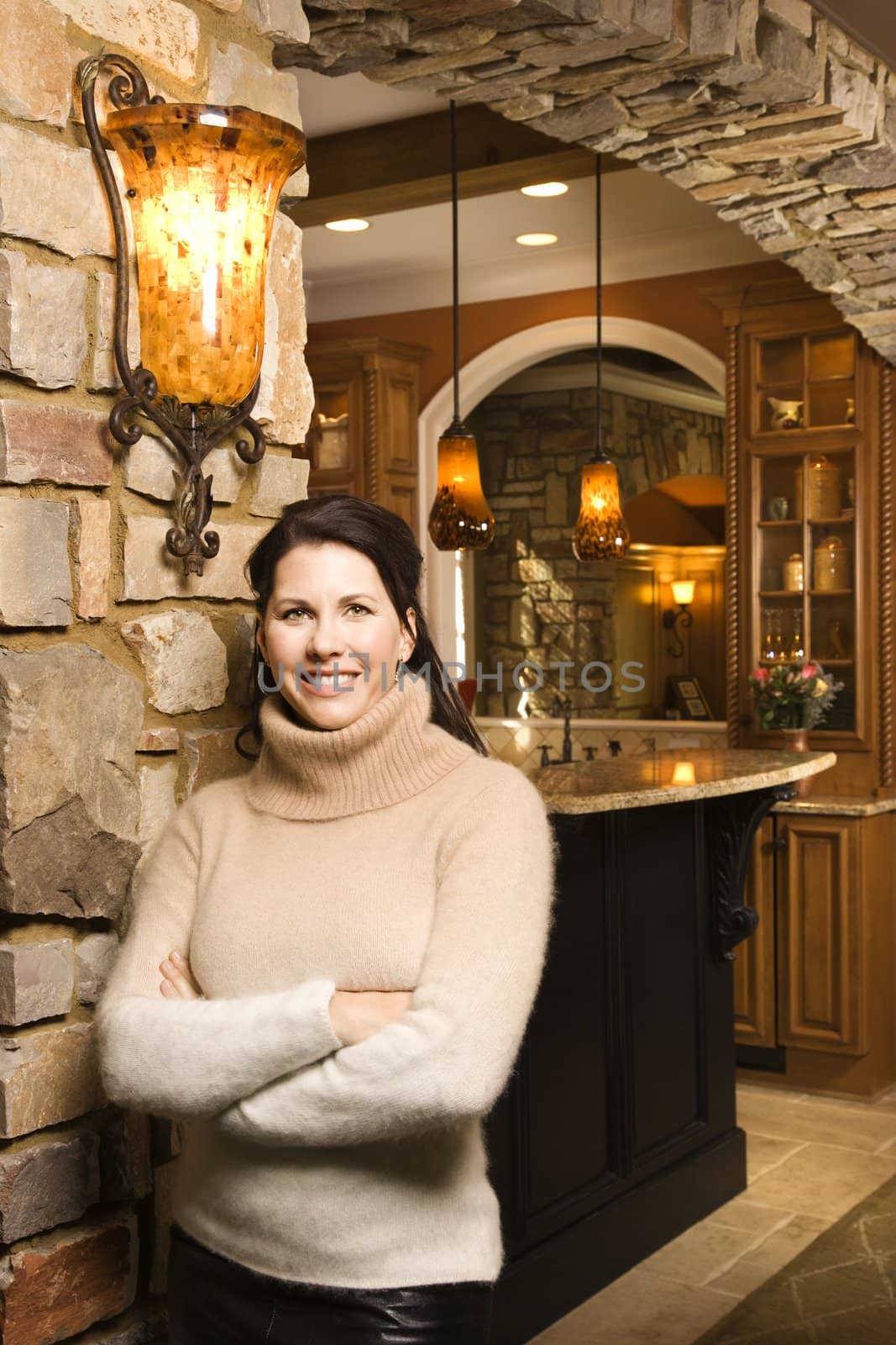 Caucasian woman standing in front of kitchen with arms crossed looking at viewer and smiling.